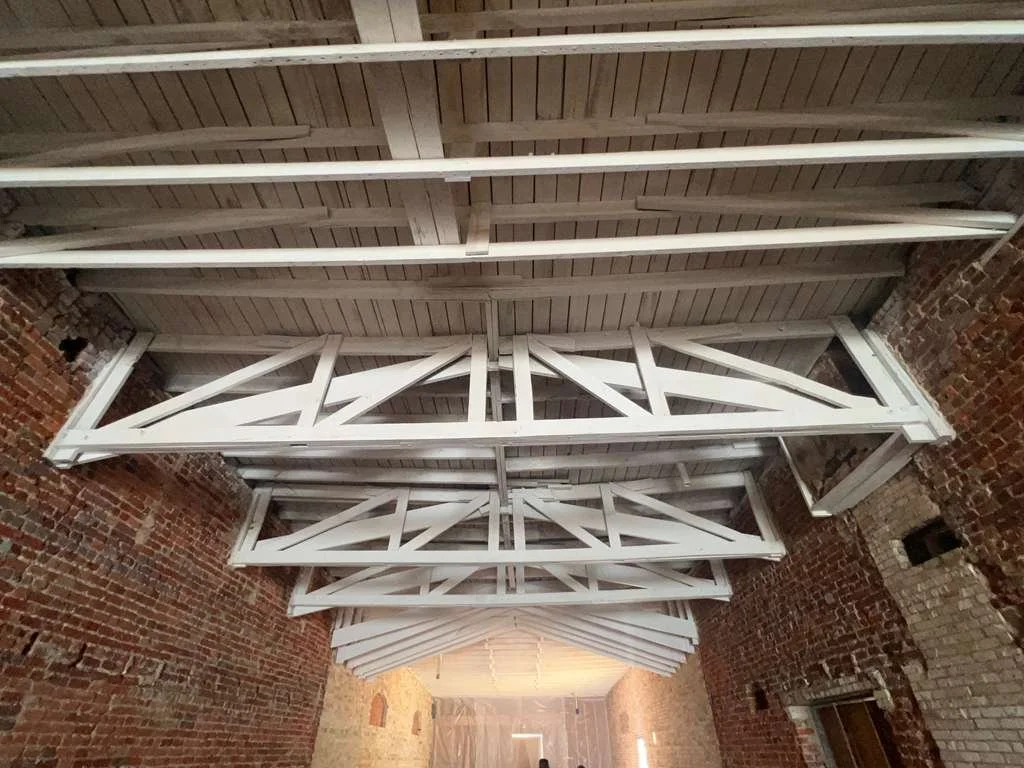 Interior view of a brick building with exposed wooden ceiling beams painted white.
