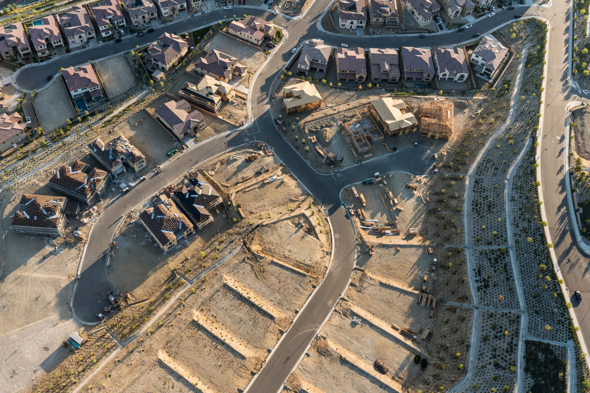 An aerial view of a residential area with multiple houses, some of which are under construction, and winding roads connecting the neighborhood.