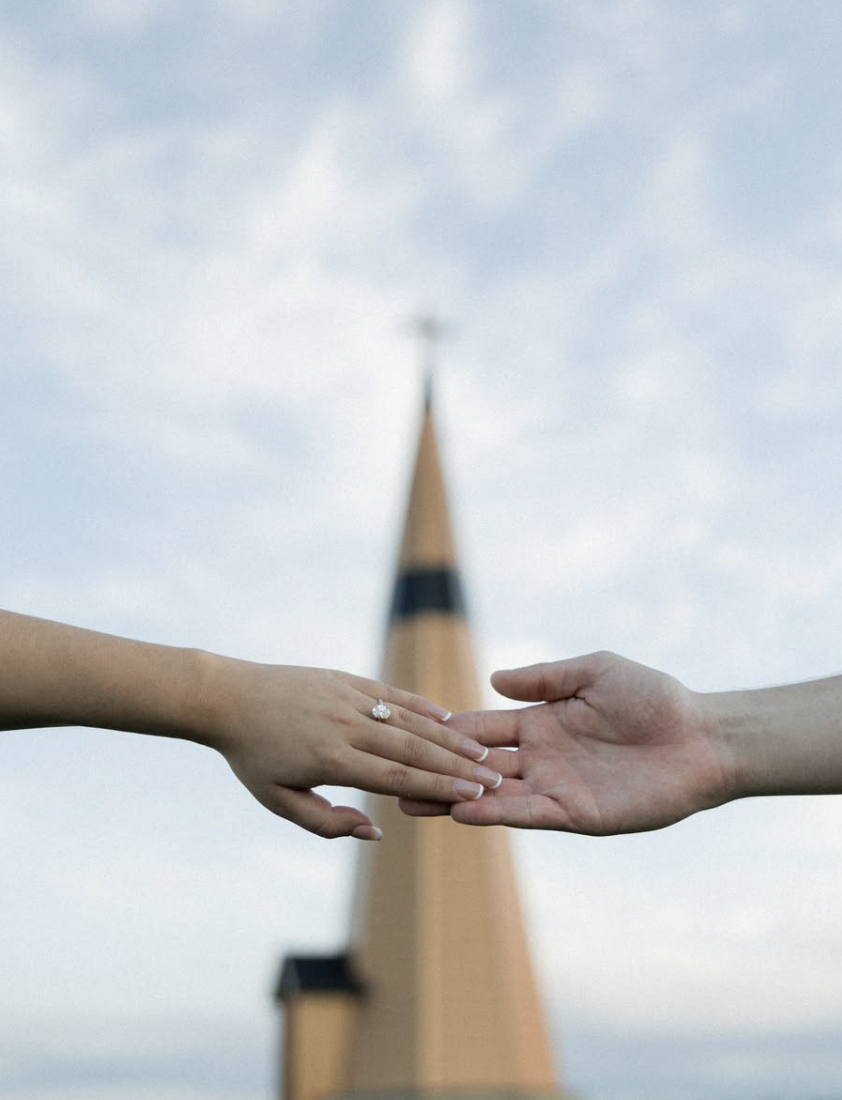 Two hands reaching towards each other with a church steeple in the background.