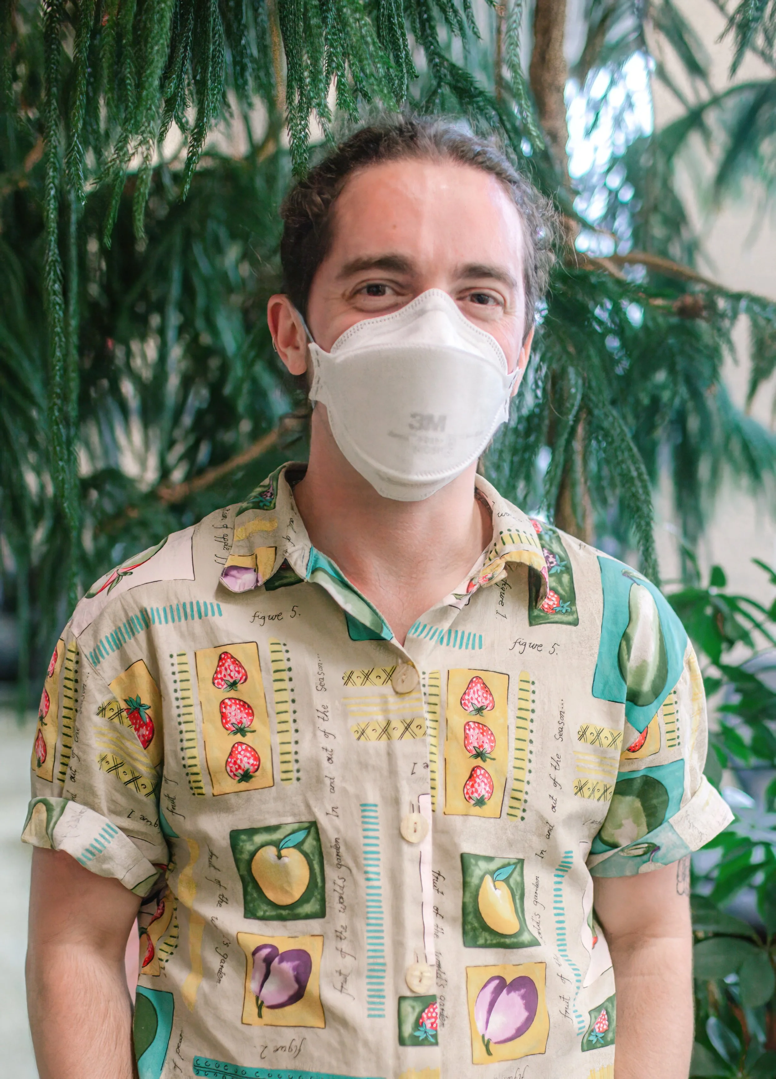 Milo, a white person with their hair pulled back, wears an N95 respirator and a tan button-down shirt