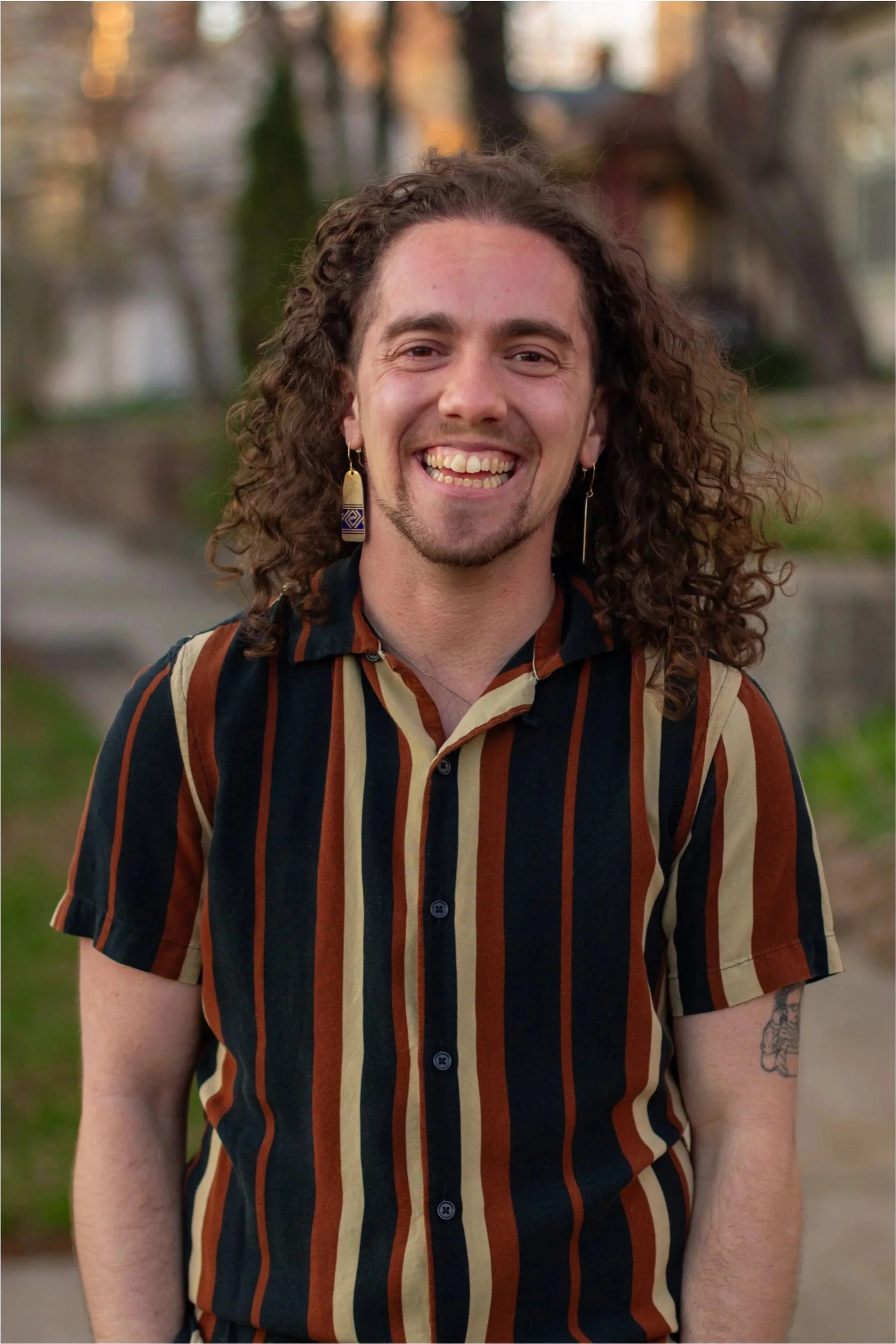 Milo, a white person with curly hair, smiles in a striped button down