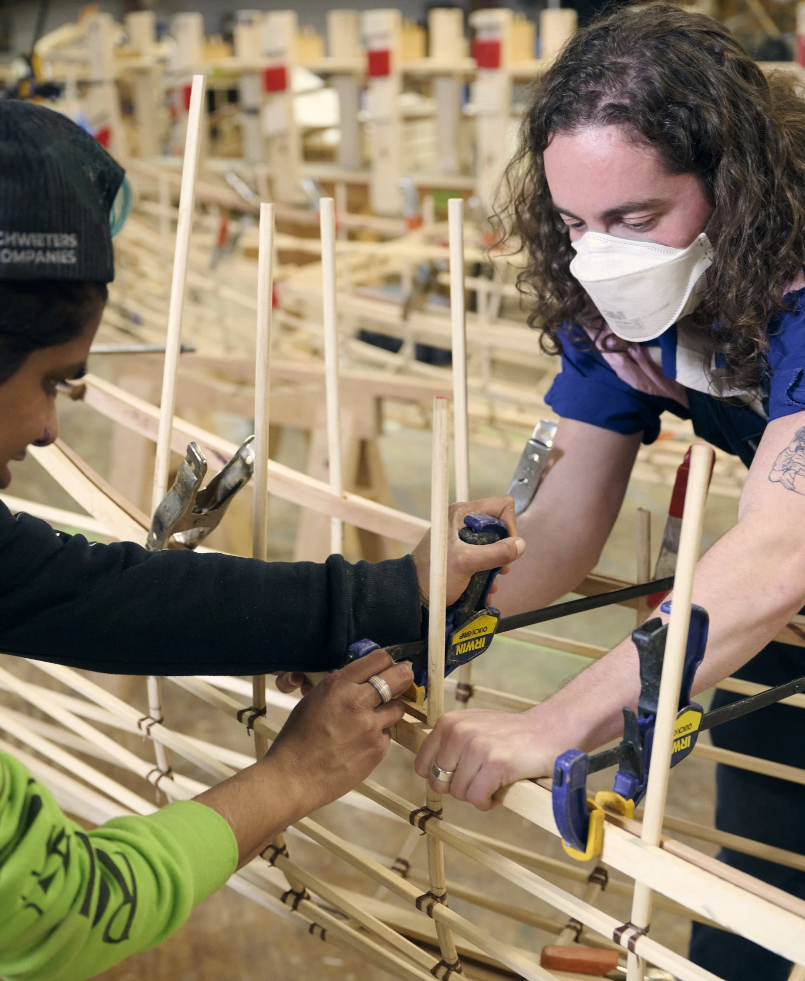 Two people work together to clamp part of a wooden canoe