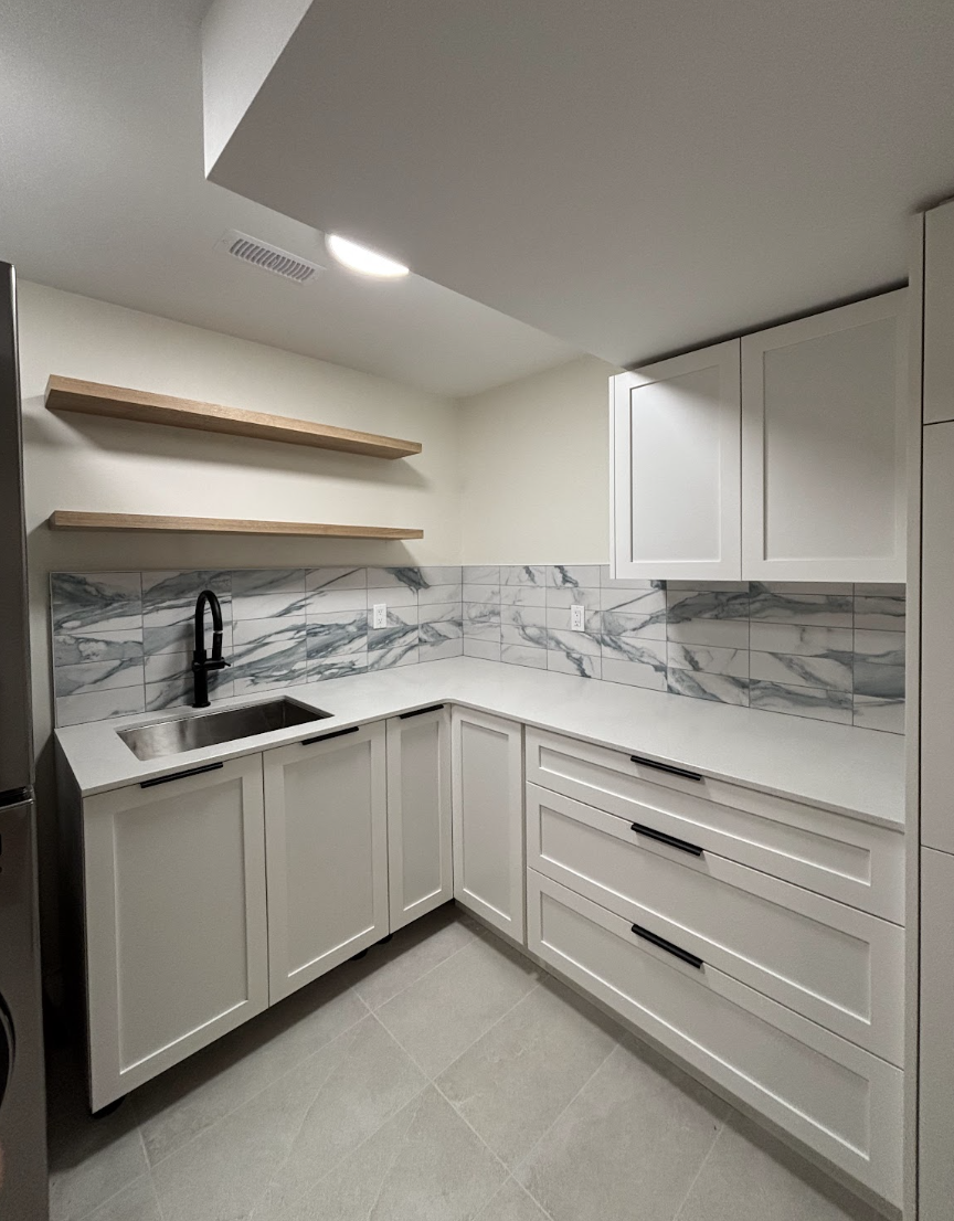 Modern kitchen with white cabinets, marble tile backsplash, black faucet, and open wooden shelves.
