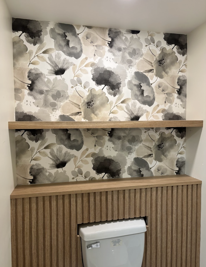 Bathroom with floral wallpaper in beige, black, and gray tones, wood shelves, and a white toilet.
