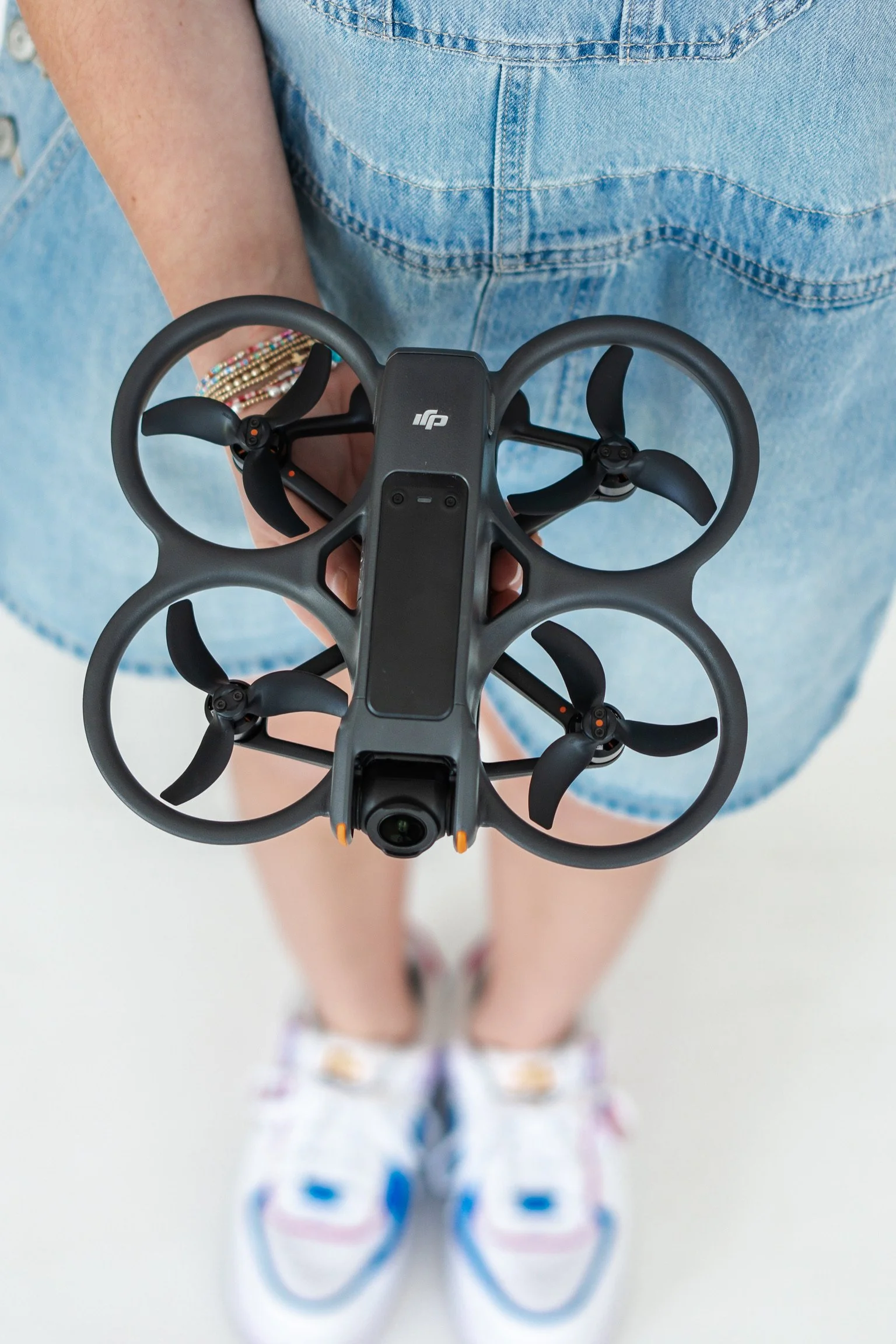 Person holding a drone while standing on a white floor, wearing colorful sneakers and denim shorts.