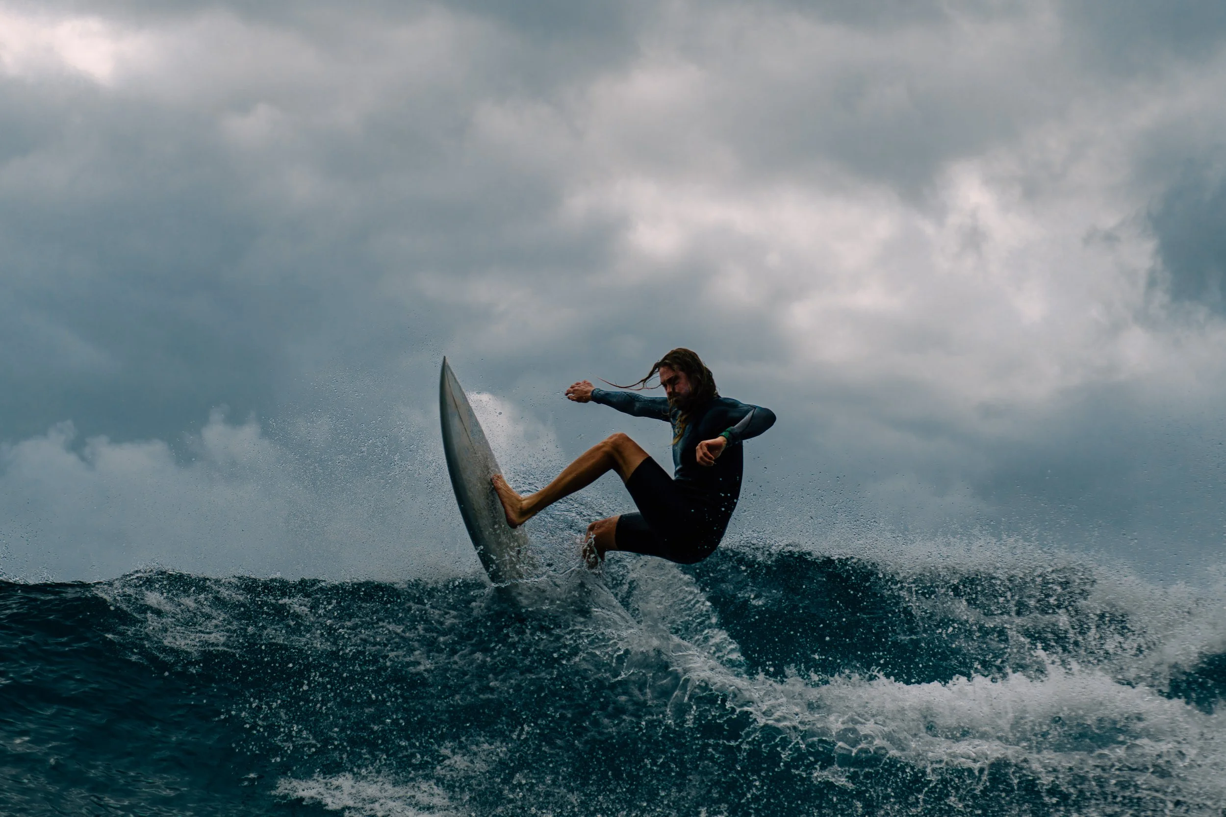 A person surfing on a wave in the ocean under cloudy skies.