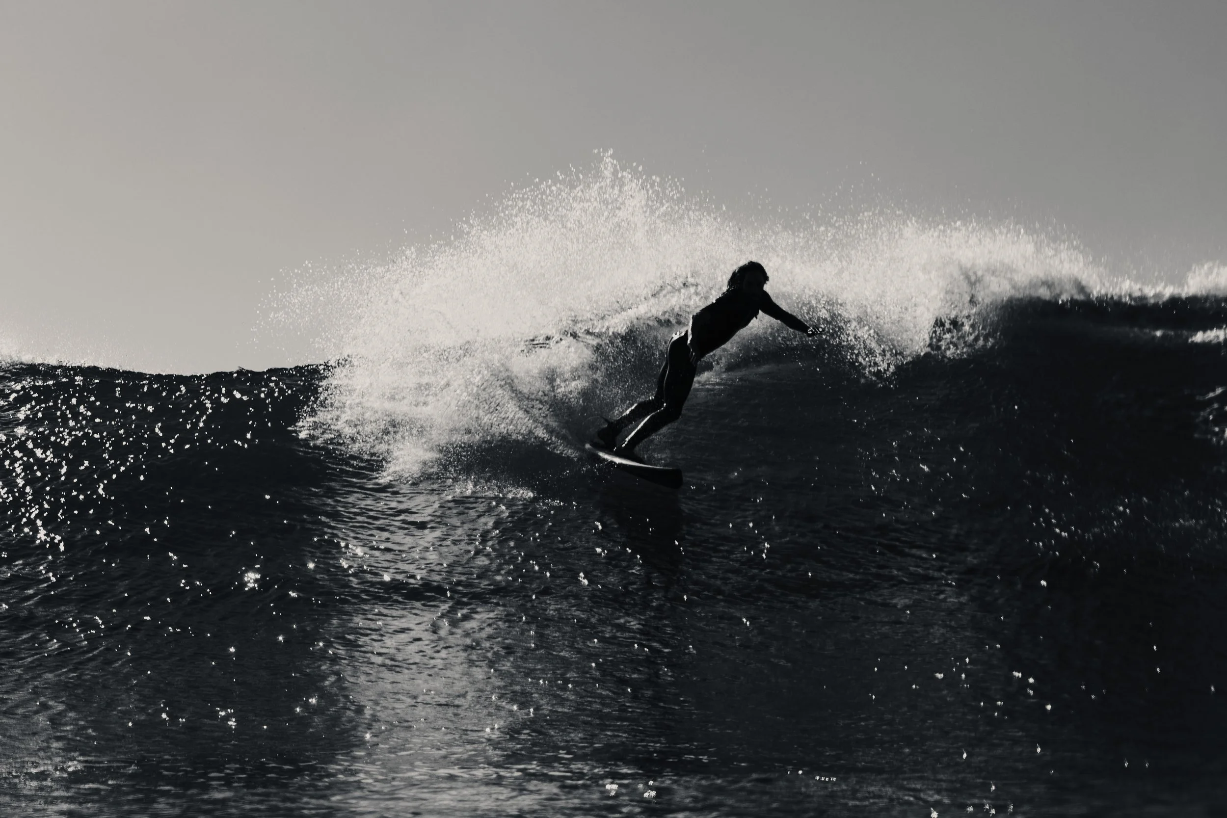 A person surfing on a wave during sunset or sunrise with silhouetted figure and spray of water.