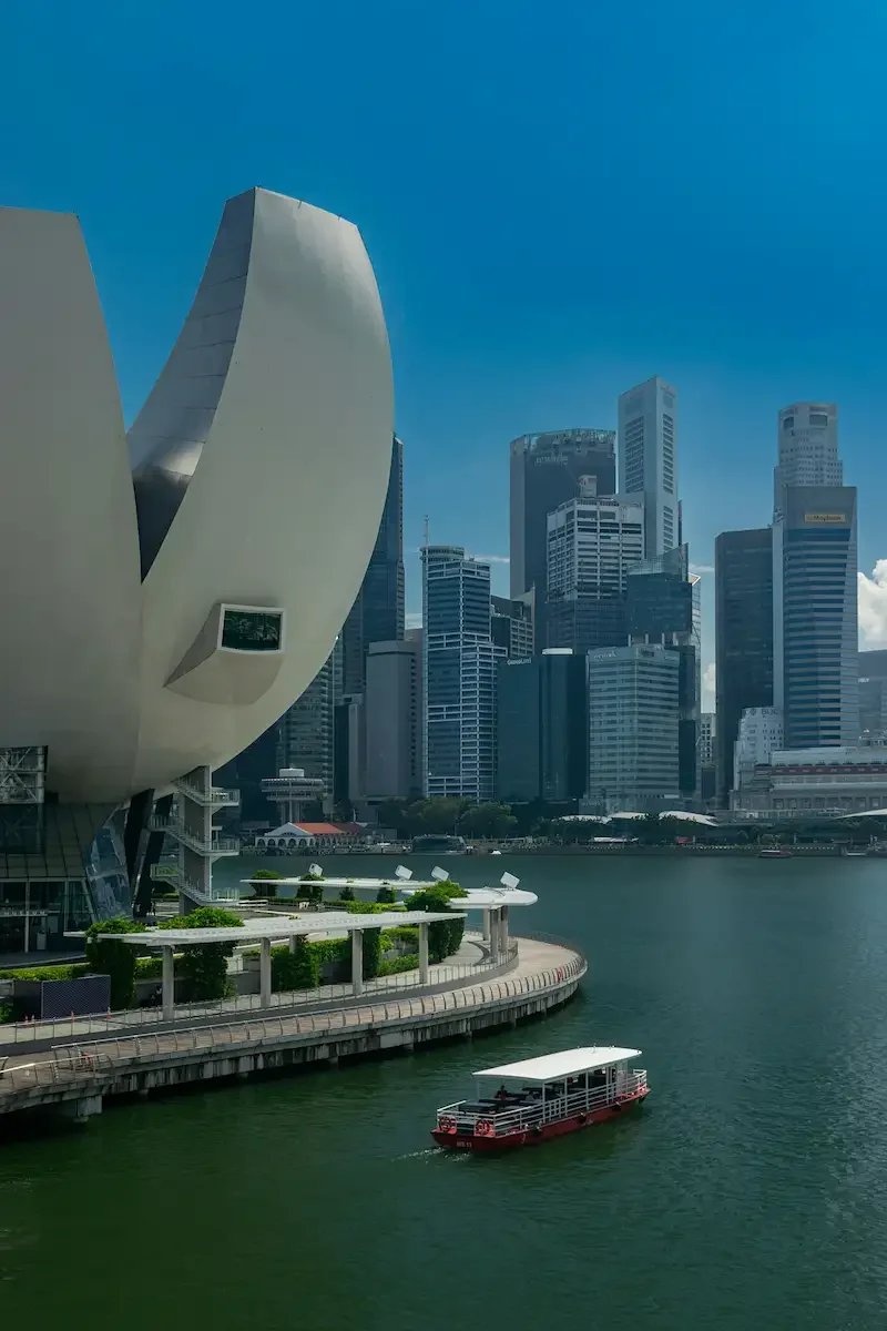 View of Marina Bay Sands hotel and city skyline in Singapore with a boat on the water in the foreground.