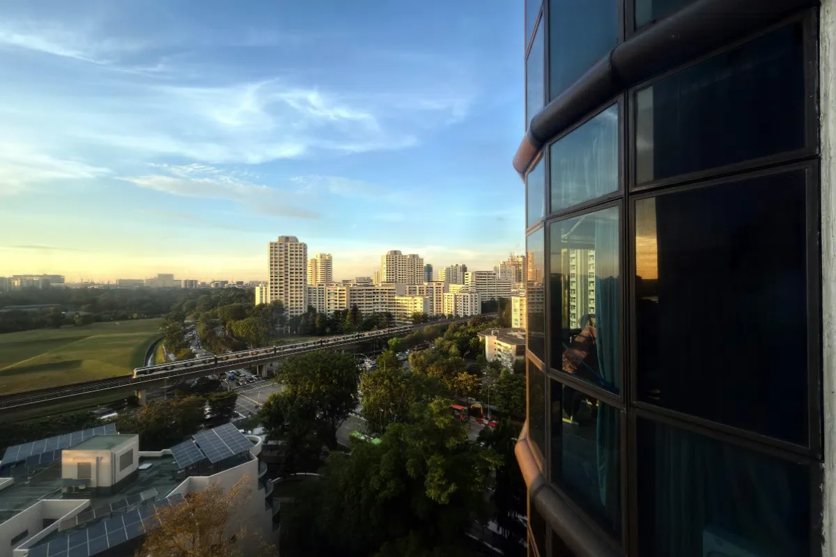 City skyline at sunset with tall office buildings, a park, and a reflection of the scene in a window on a building's exterior.