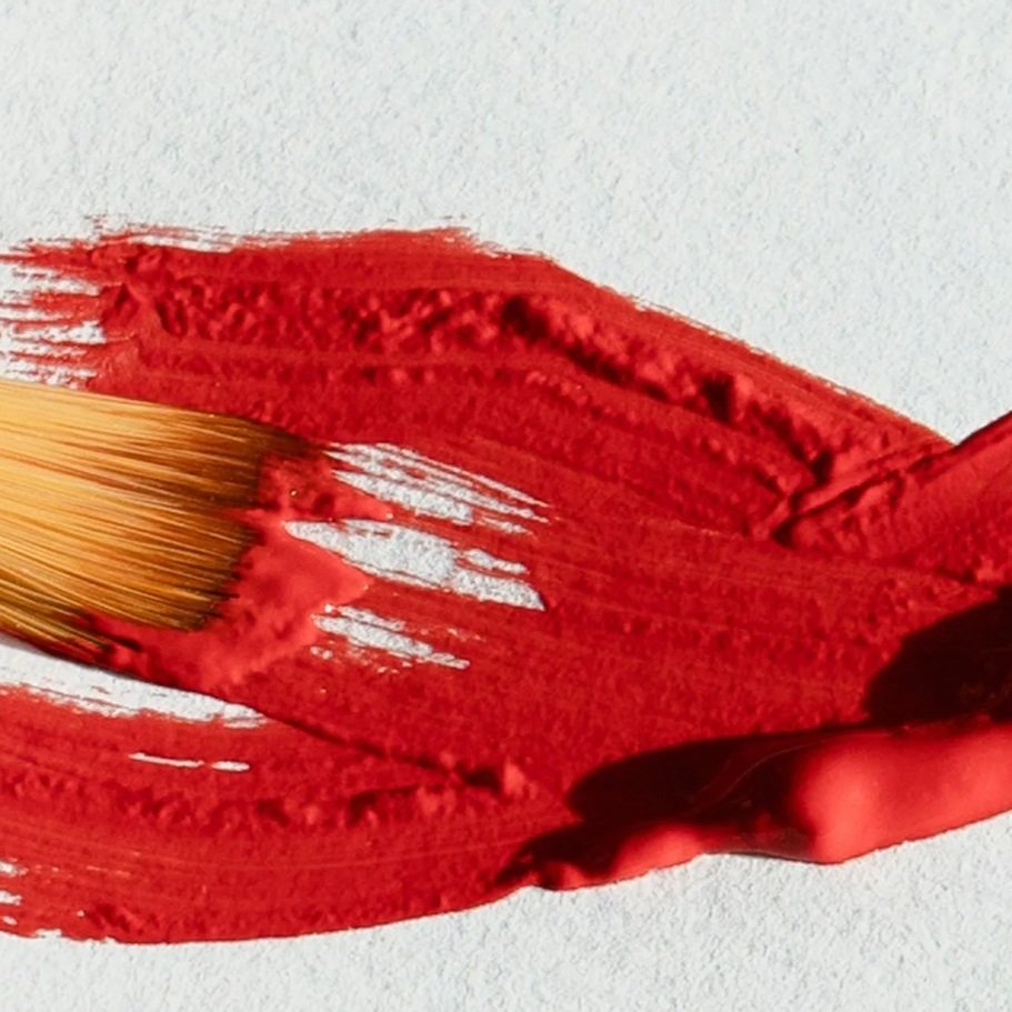 Paintbrush with red paint stroke on white paper.