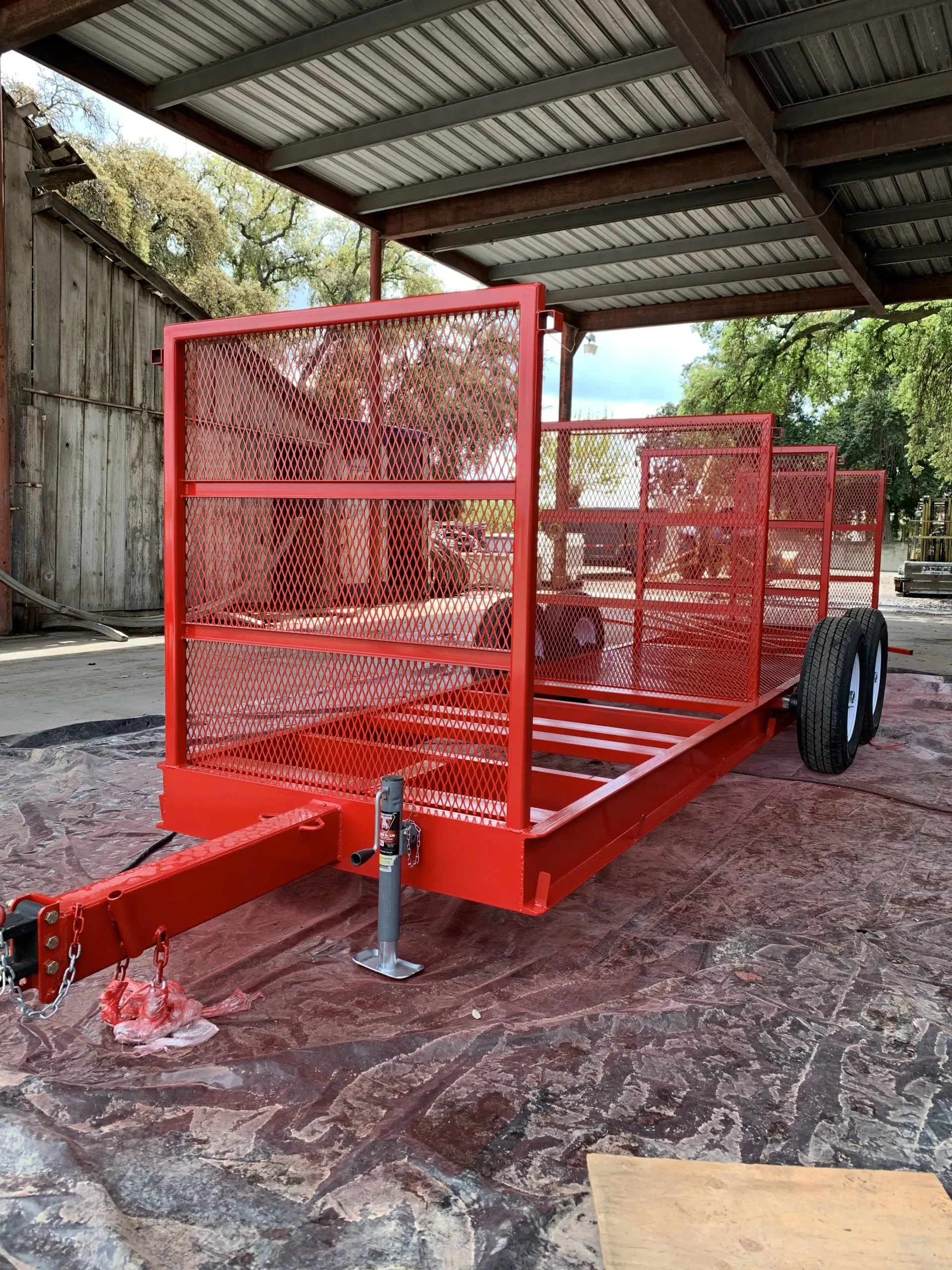 A red utility trailer with mesh sides parked inside a covered area, showing an example of an industrial coating for agricultural equipment.