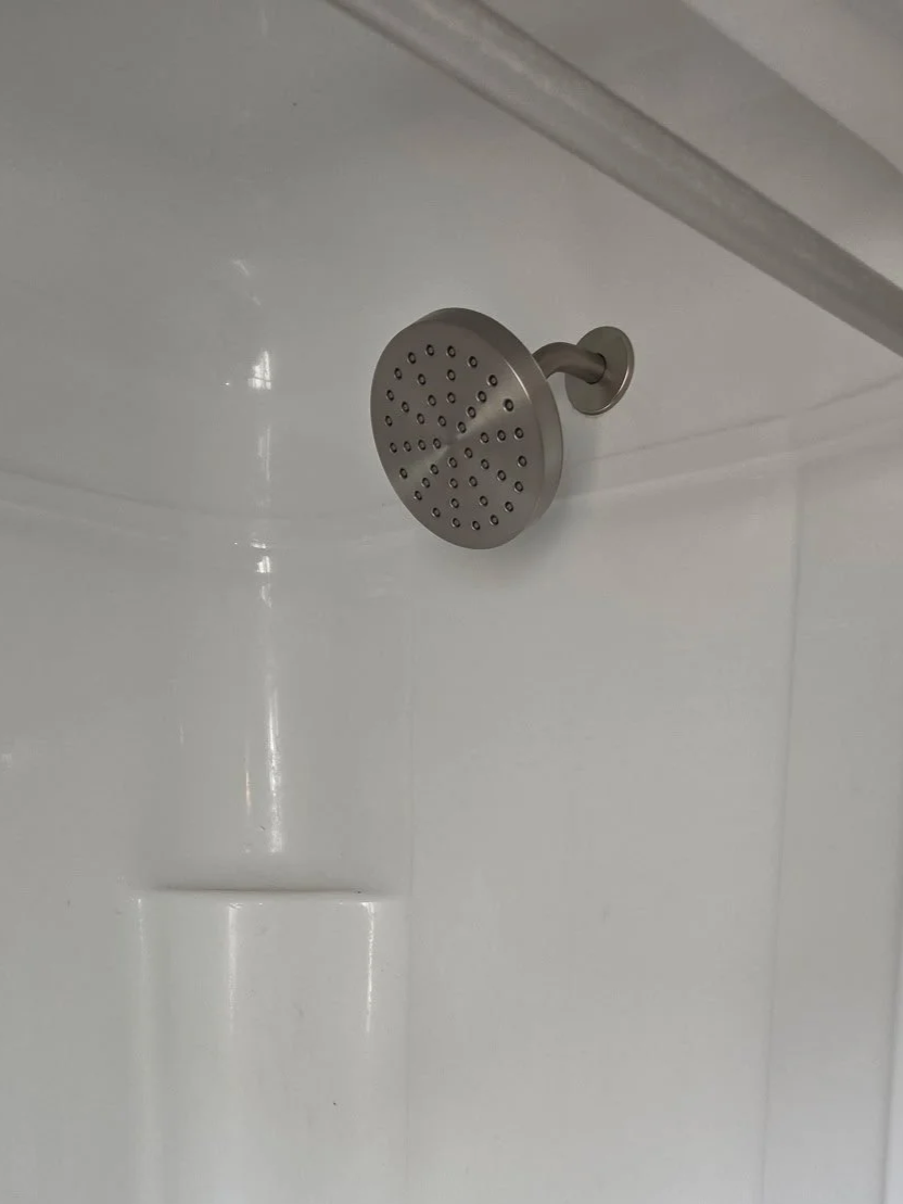 A metal showerhead mounted on a white shower wall.