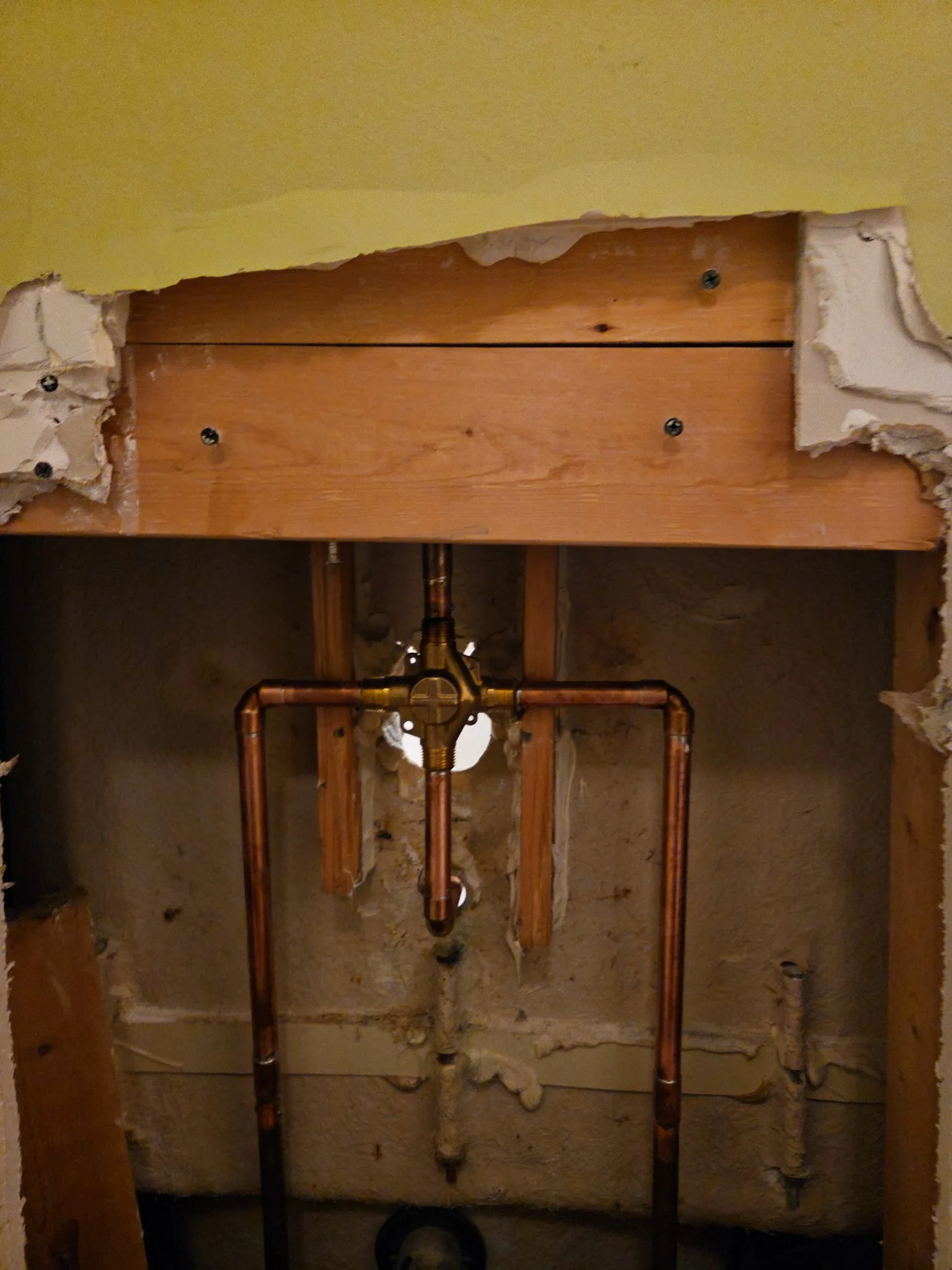 View of a bathroom wall with exposed wooden framing, copper water pipes, and insulation material.