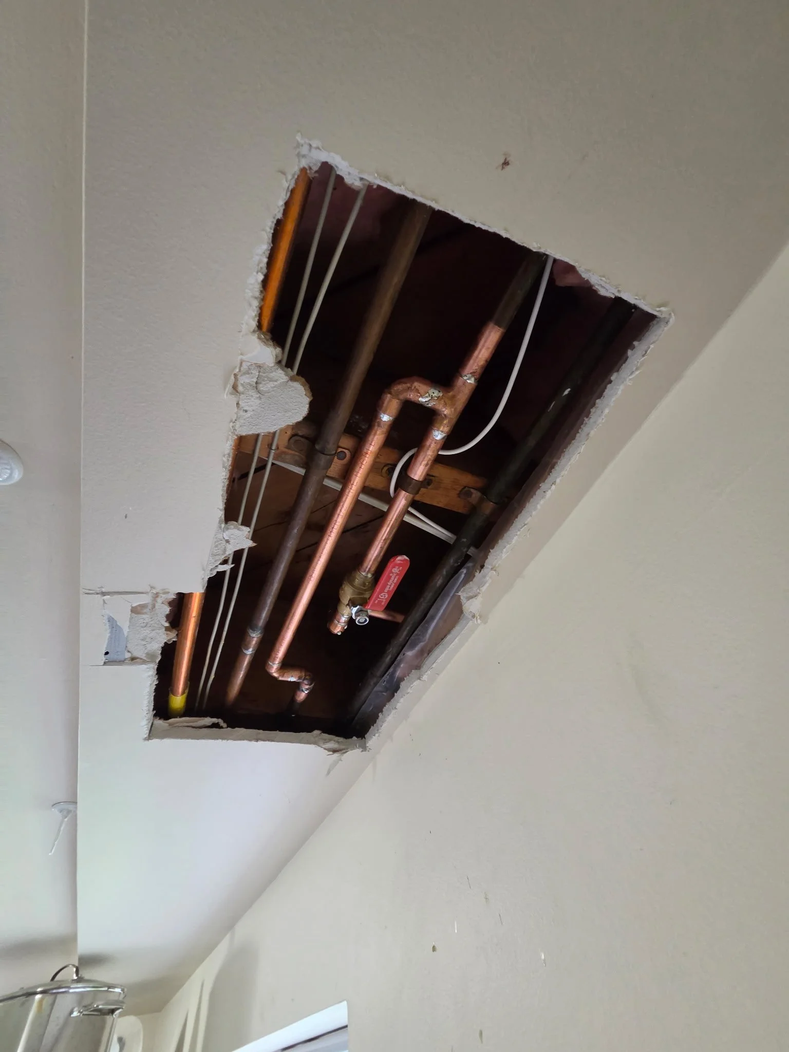Ceiling with a large hole exposing plumbing pipes and electrical wires behind the drywall.