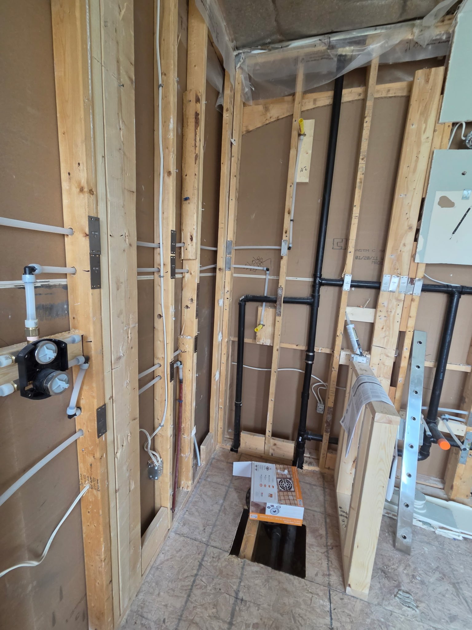 Construction area with exposed wooden framing, electrical wiring, plumbing pipes, and construction equipment. The space appears to be in the process of being remodeled or built.