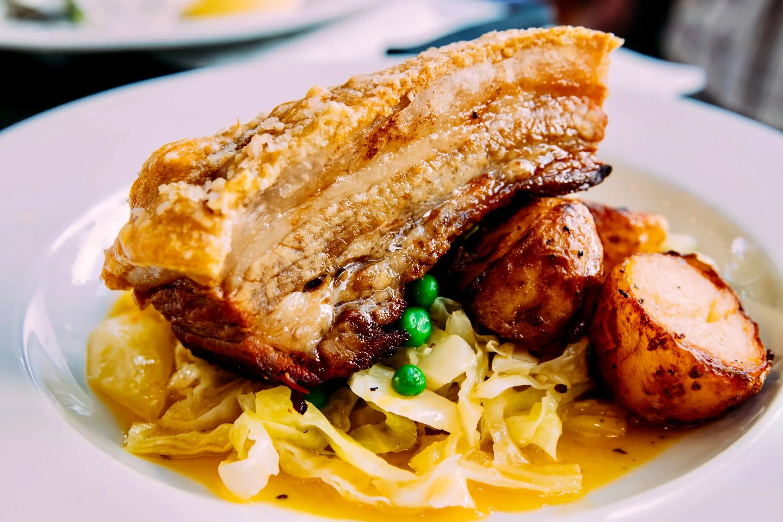 Close-up of a plated serving of roast meat with a crispy crust, topped with peas, served over cabbage and potatoes.