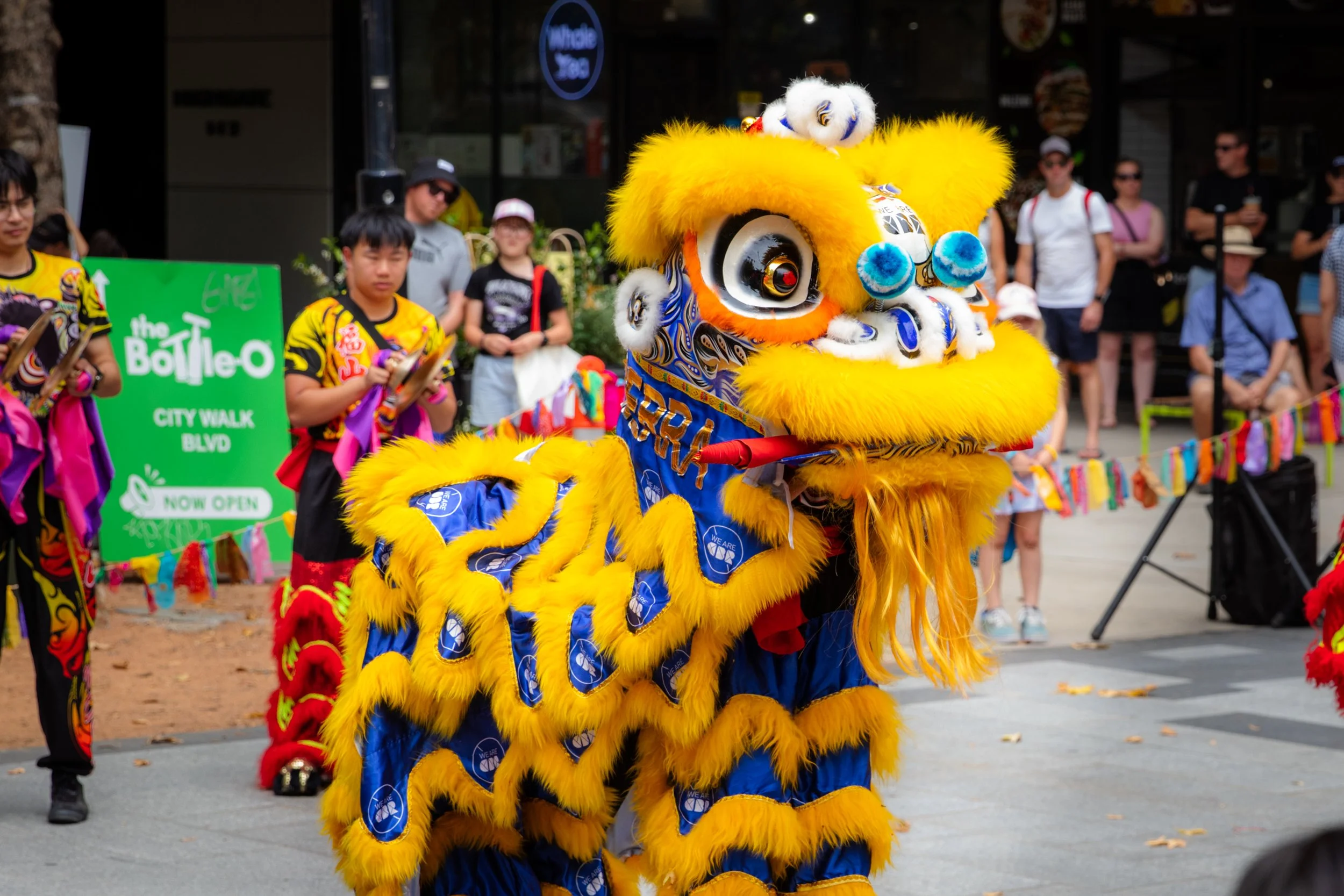 Yellow lion dance costume at a parade with people watching in the background.