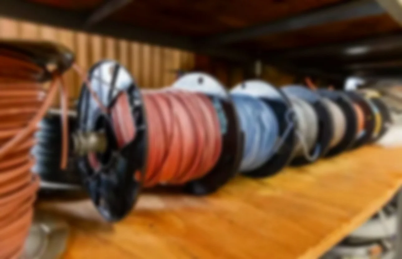 A collection of electrical extension cords coiled on a wooden workbench, with various colors and sizes, stored on black spools.