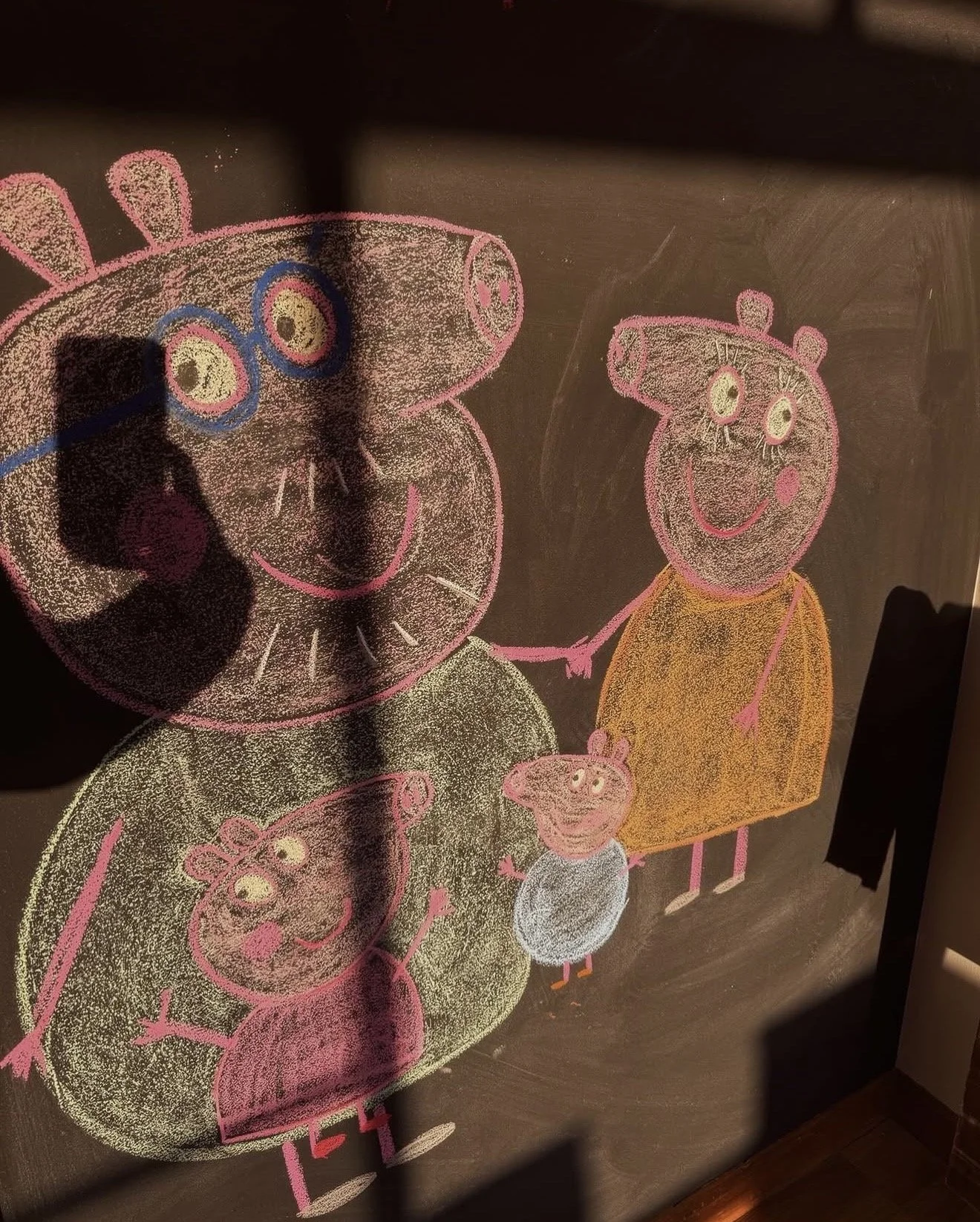 Colorful chalk drawing of Peppa Pig family holding hands, with Peppa Pig, George, and their family members on a blackboard.