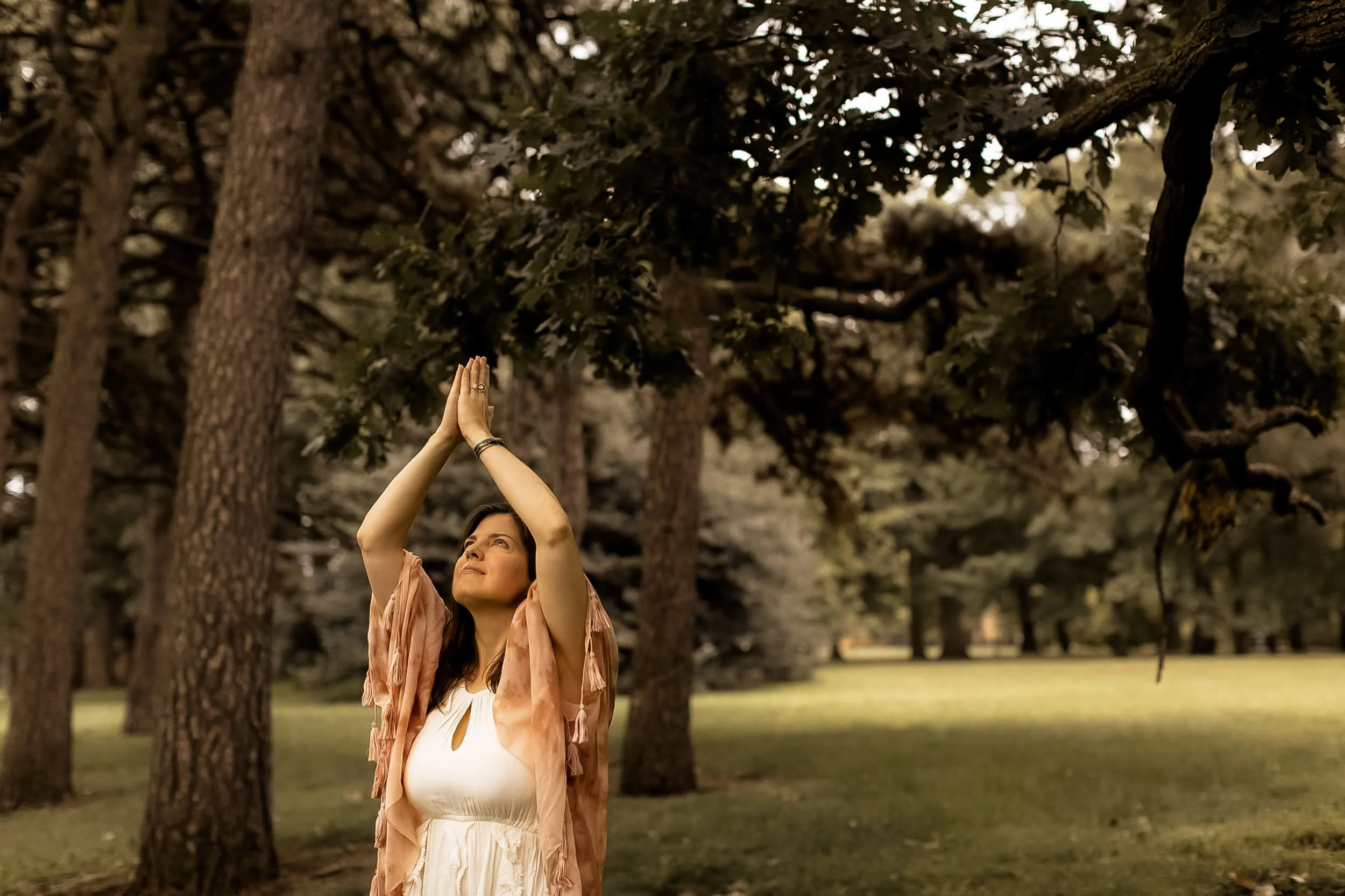 Kristi Amdahl with prayer hands above her head by a bunch of trees