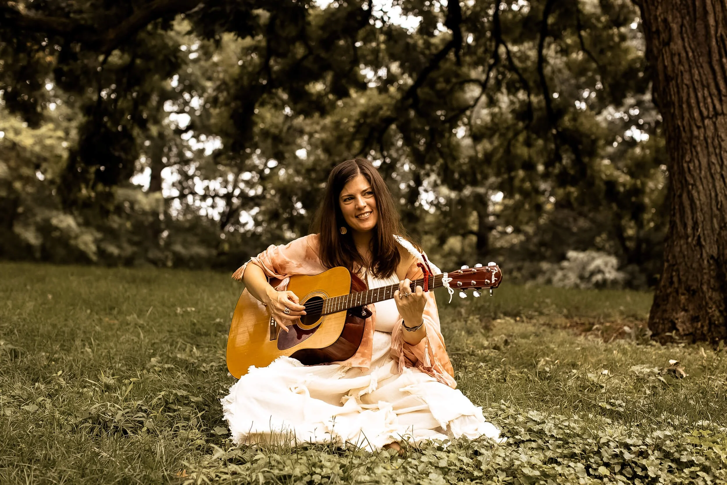 Kristi sitting in a field playing her guitar and smiling