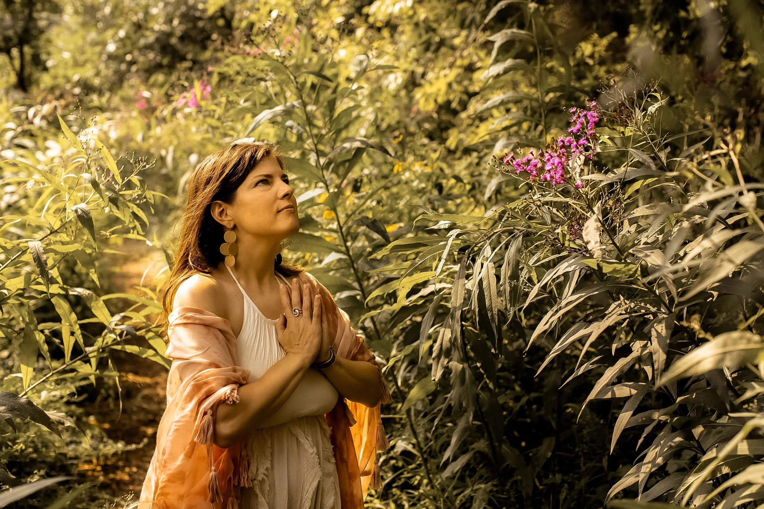 Kristi with prayer hands while surrounded by plants