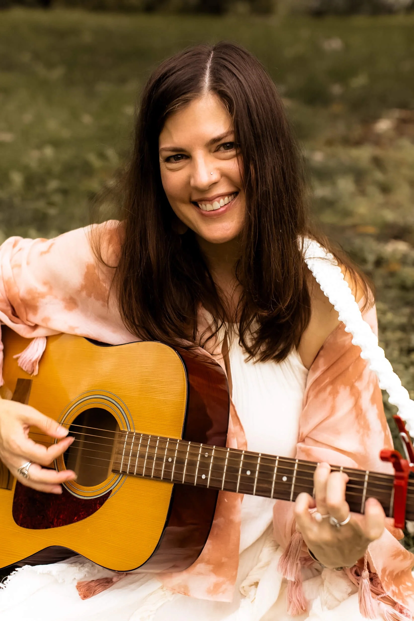 Kristi smiling at the camera while playing her guitar