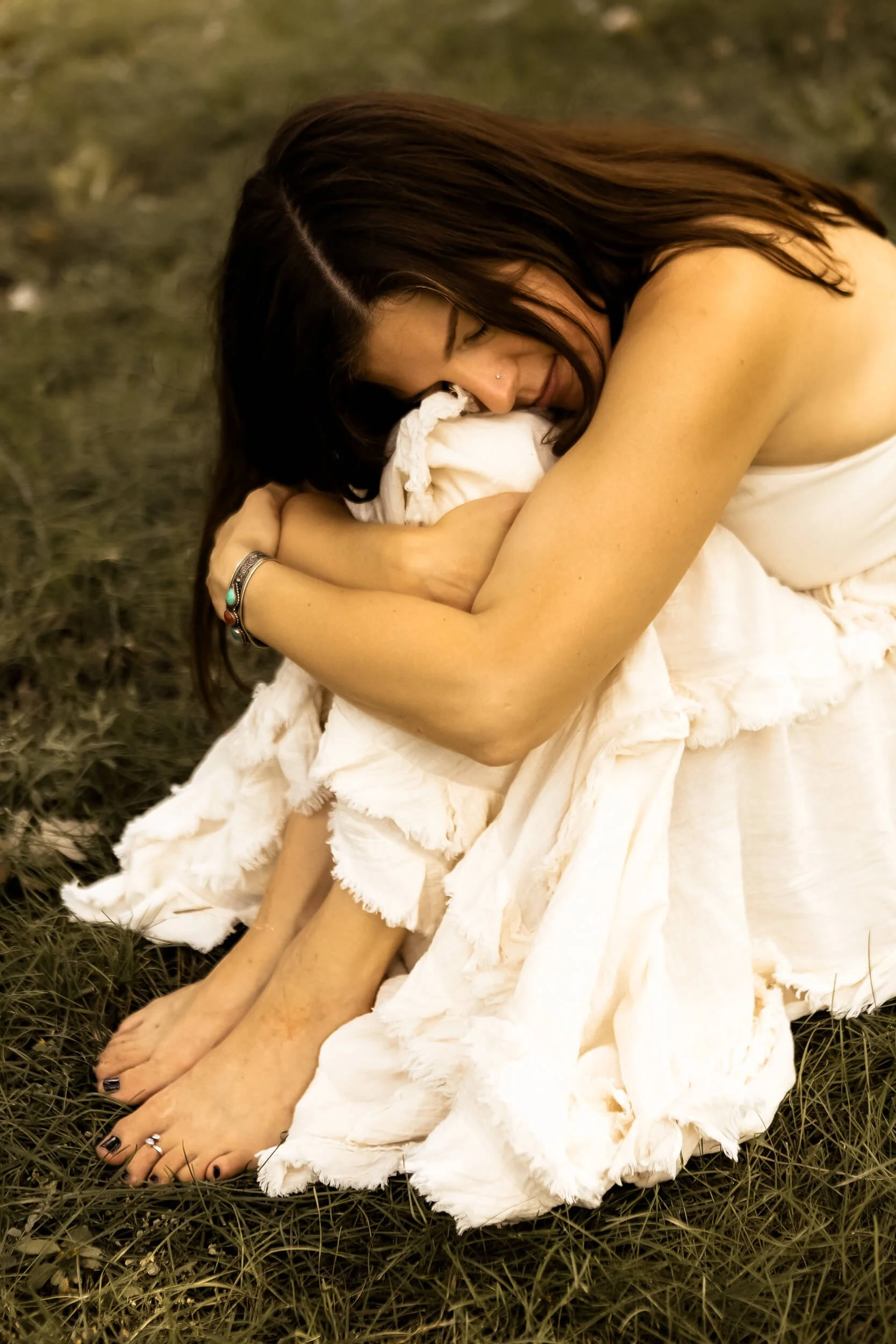 Kristi hugging her knees while sitting in the grass close-up