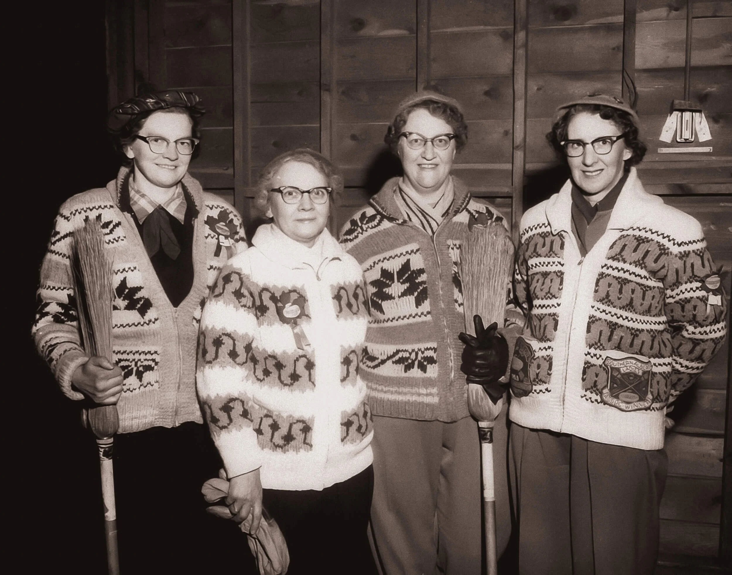 vintage photo of four women holding brooms and looking a tad bit devious