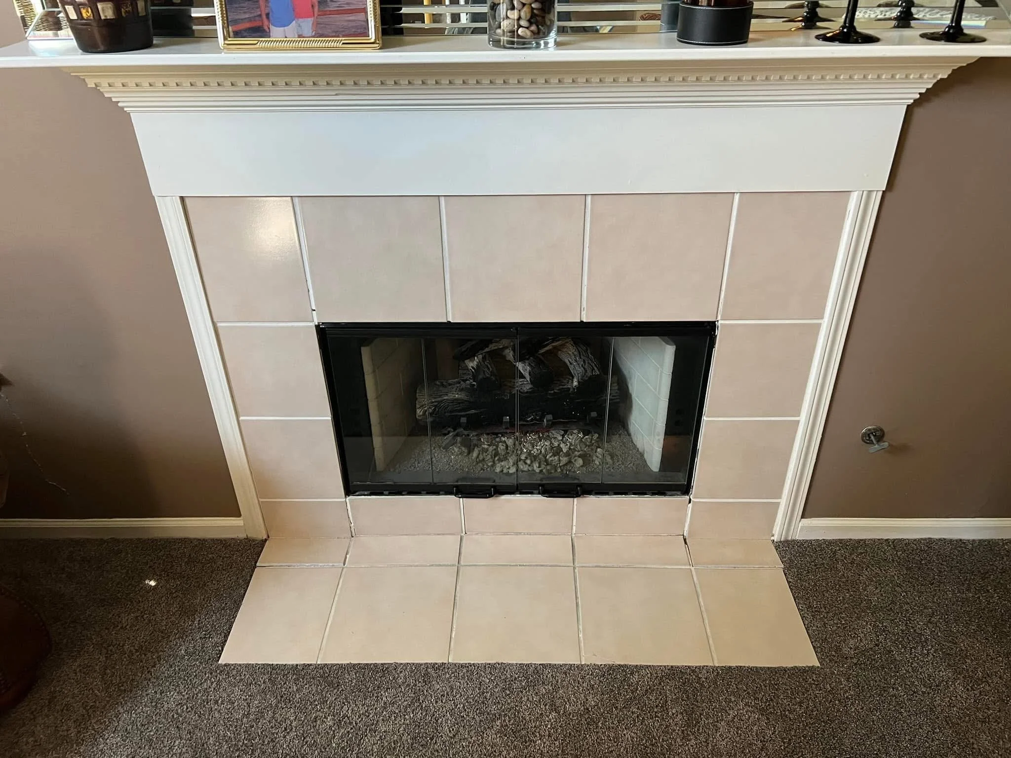 Fireplace with beige tile surround and a white mantel, decorated with framed photographs, vases, and candle holders.
