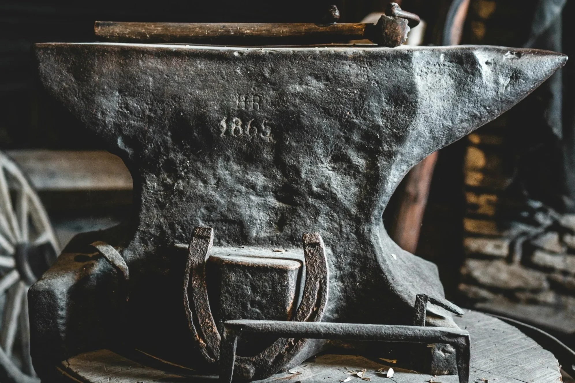Close-up of an old, rusted metal anvil with markings and a hammer resting on top, in a workshop.