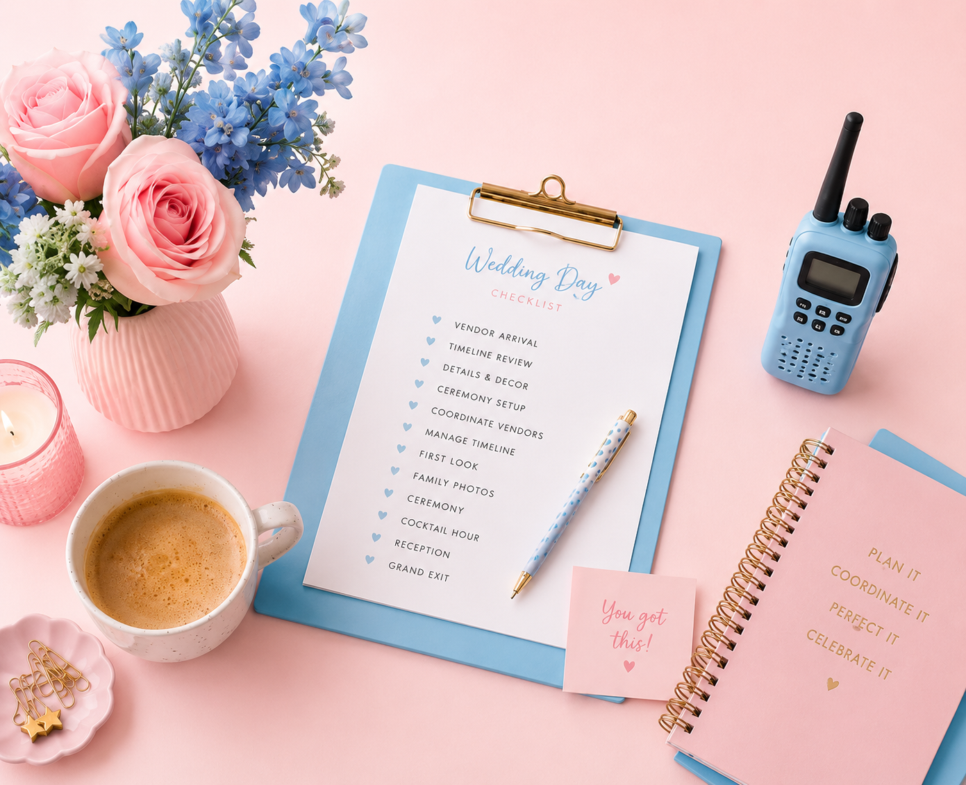 Wedding planning desk with a pink and blue color theme, featuring a flower vase with pink roses and blue flowers, a wedding checklist on a clipboard, a walkie-talkie, a pink planner, a pink notebook, a cup of coffee, a candle, gold paper clips, and a note saying "You got this!"