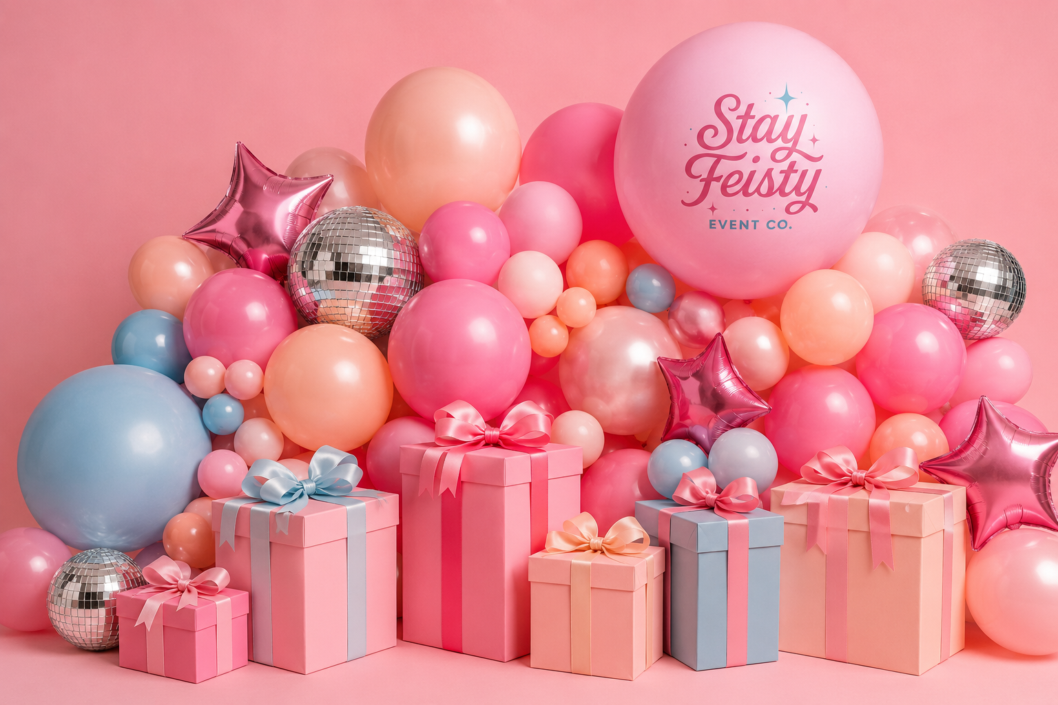 A colorful balloon backdrop with pink, blue, peach, and silver balloons, some star-shaped, along with wrapped gift boxes in pastel colors, and a large pink balloon with the text Stay Feisty Event Co.