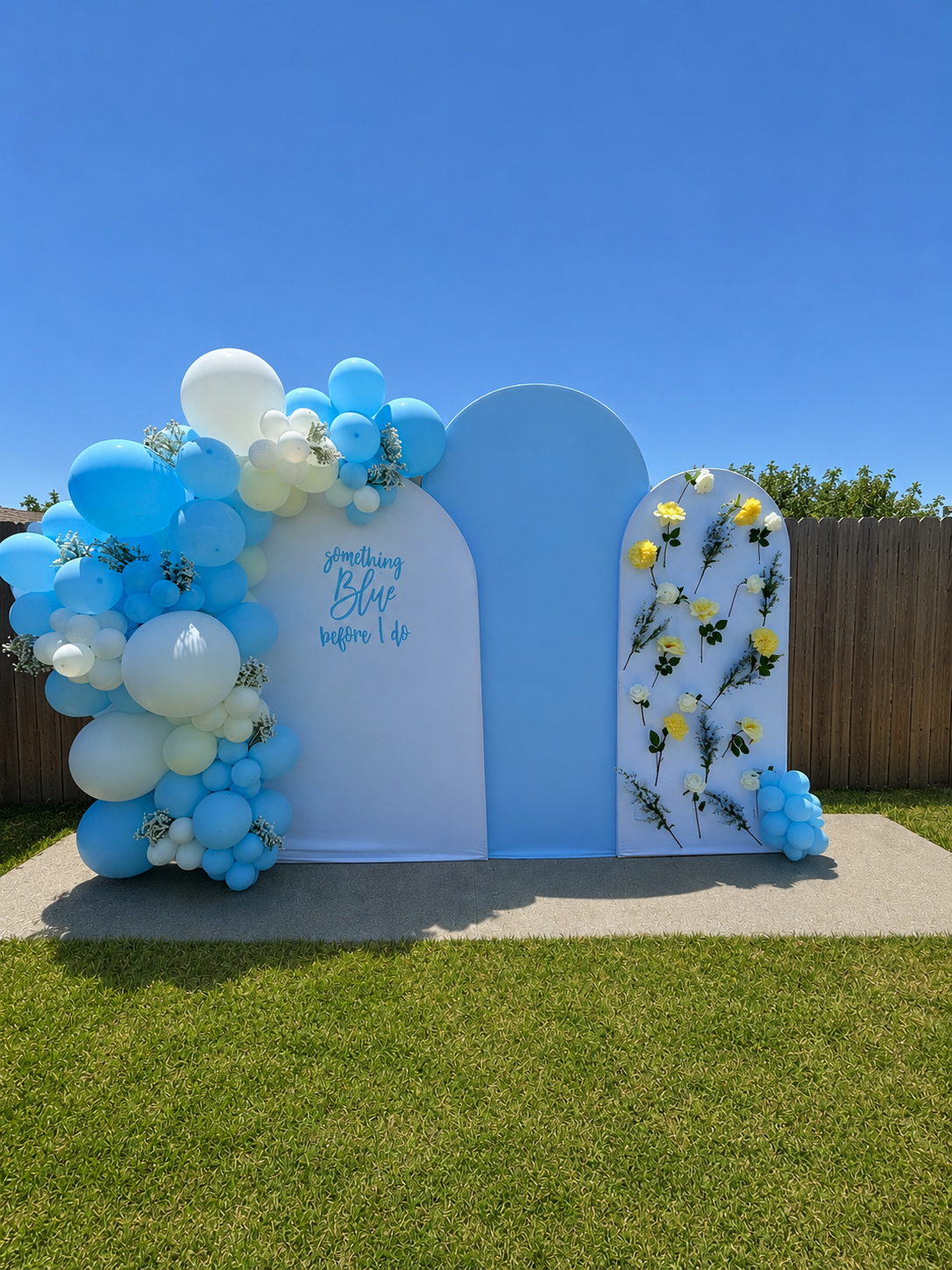 Backyard outdoor decoration with three panels, blue background, yellow and white flowers, and blue and white balloons on a sunny day.