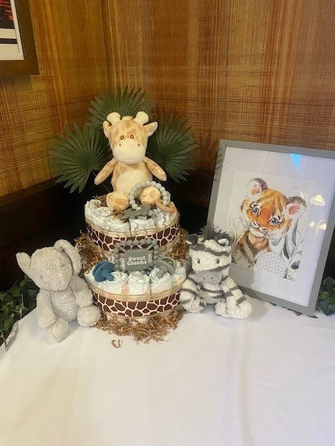 Decorative display with plush toys of a giraffe and two baby tigers, a framed picture of a tiger cub, and a cake with stuffed animals on top, set against a wooden-paneled wall.