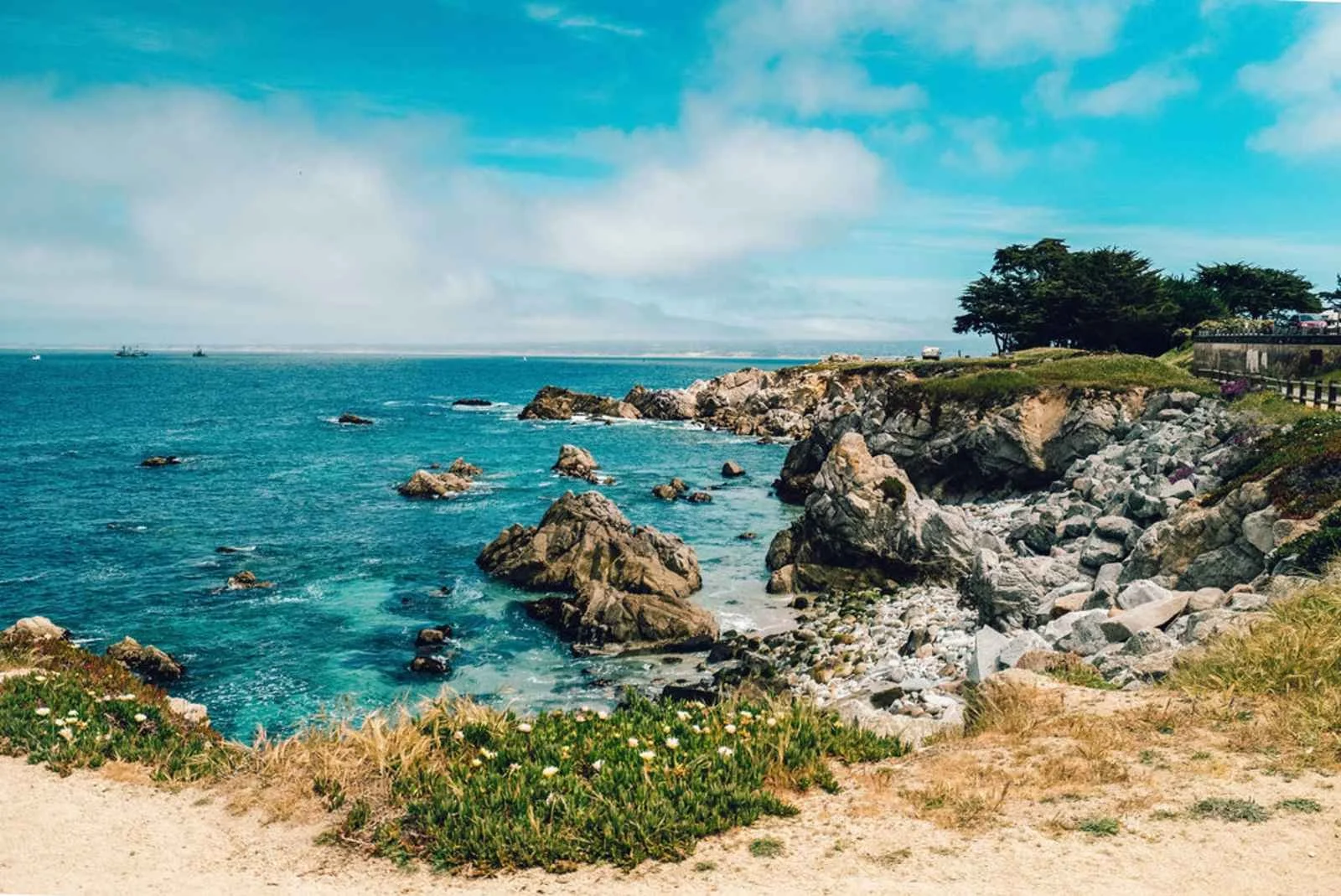 Coastal scene with rocky shoreline, blue ocean, and clear sky with some clouds.