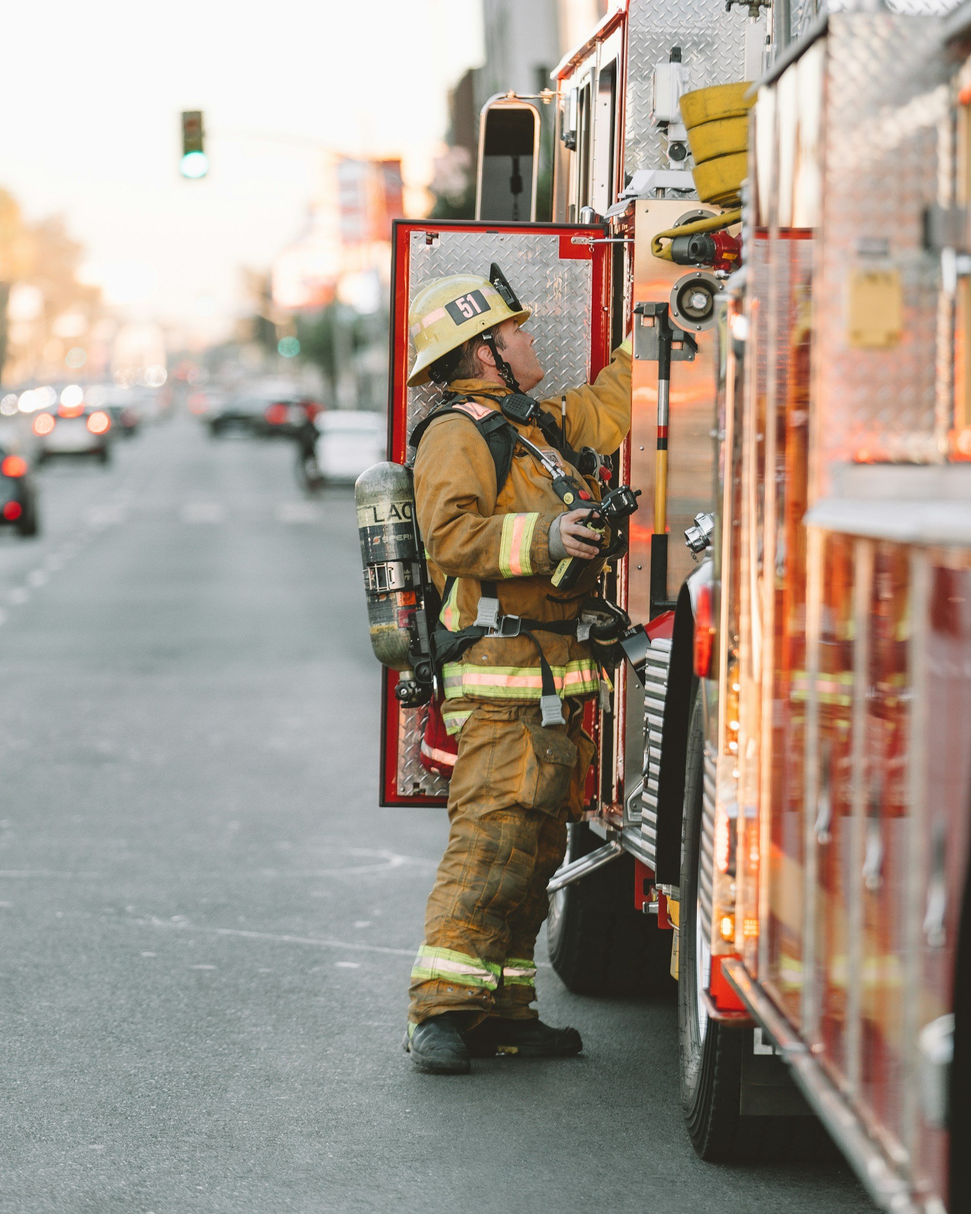 A firefighter in turnout gear, helmet, and breathing apparatus working on a fire truck