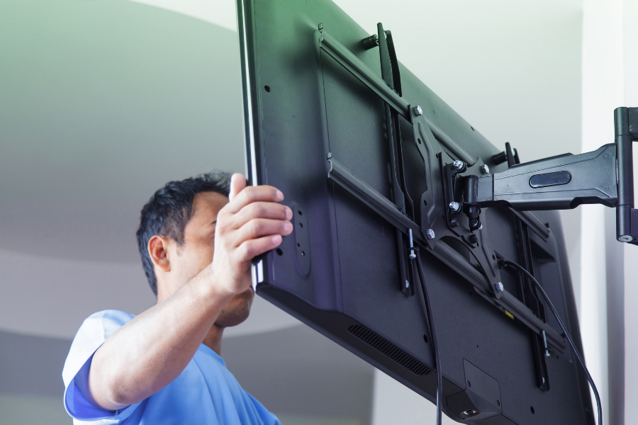 A person installing or mounting a flat screen television to a wall with a mounting bracket.