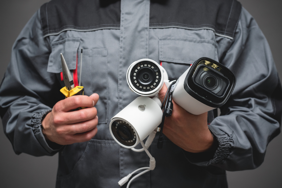 Person in gray work jacket holding surveillance cameras and tools