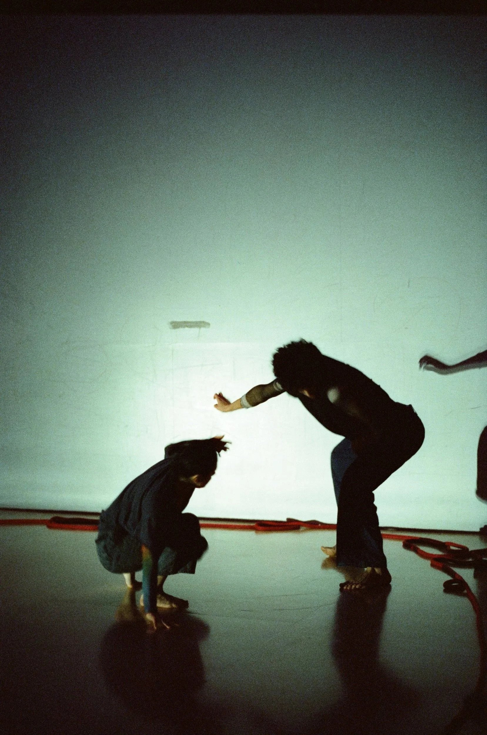 Children playing and crawling on the floor in a dark room with a lit wall, casting shadows of their figures.