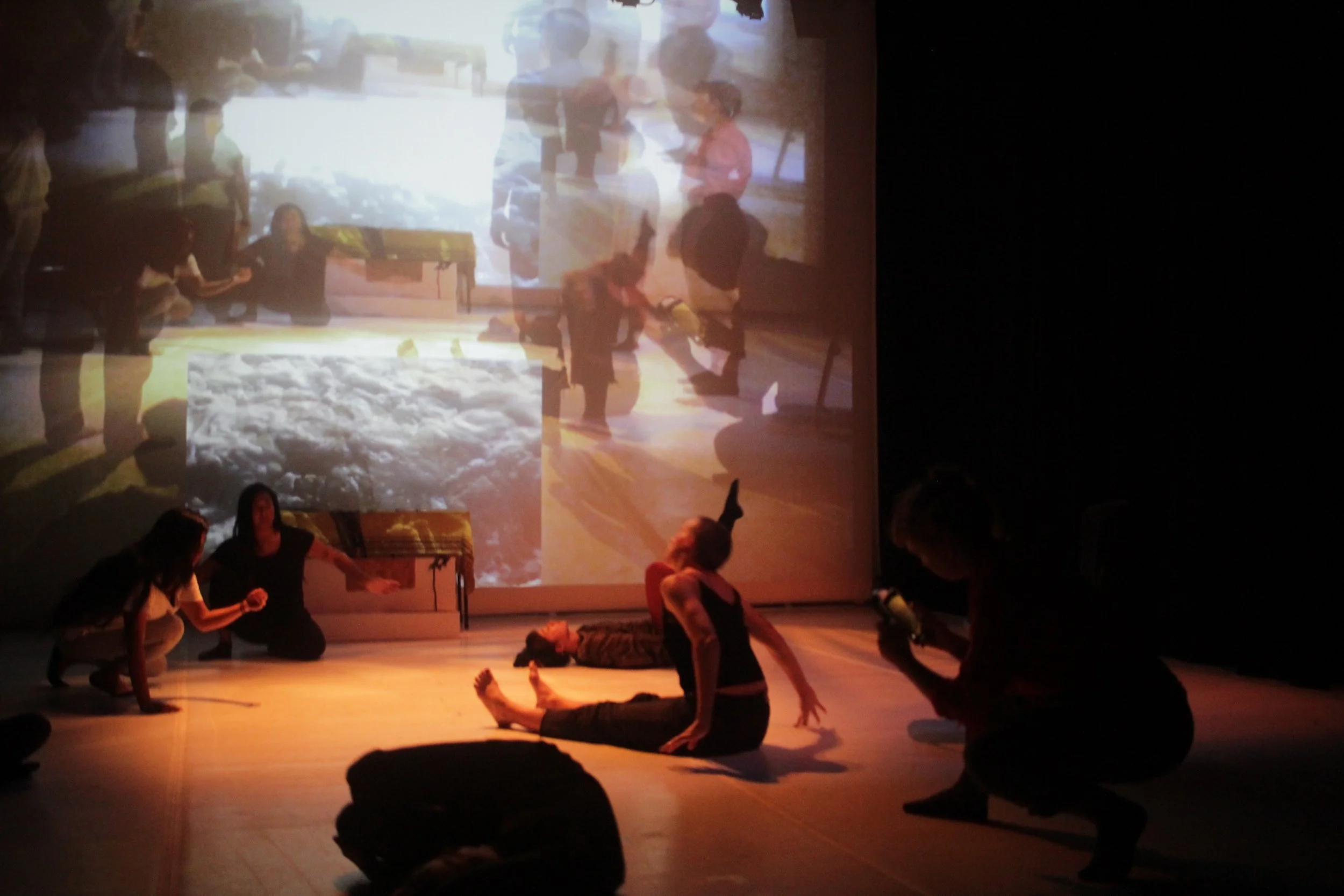 People practicing yoga in a dimly lit room with a large projection of a cityscape on the wall behind them.