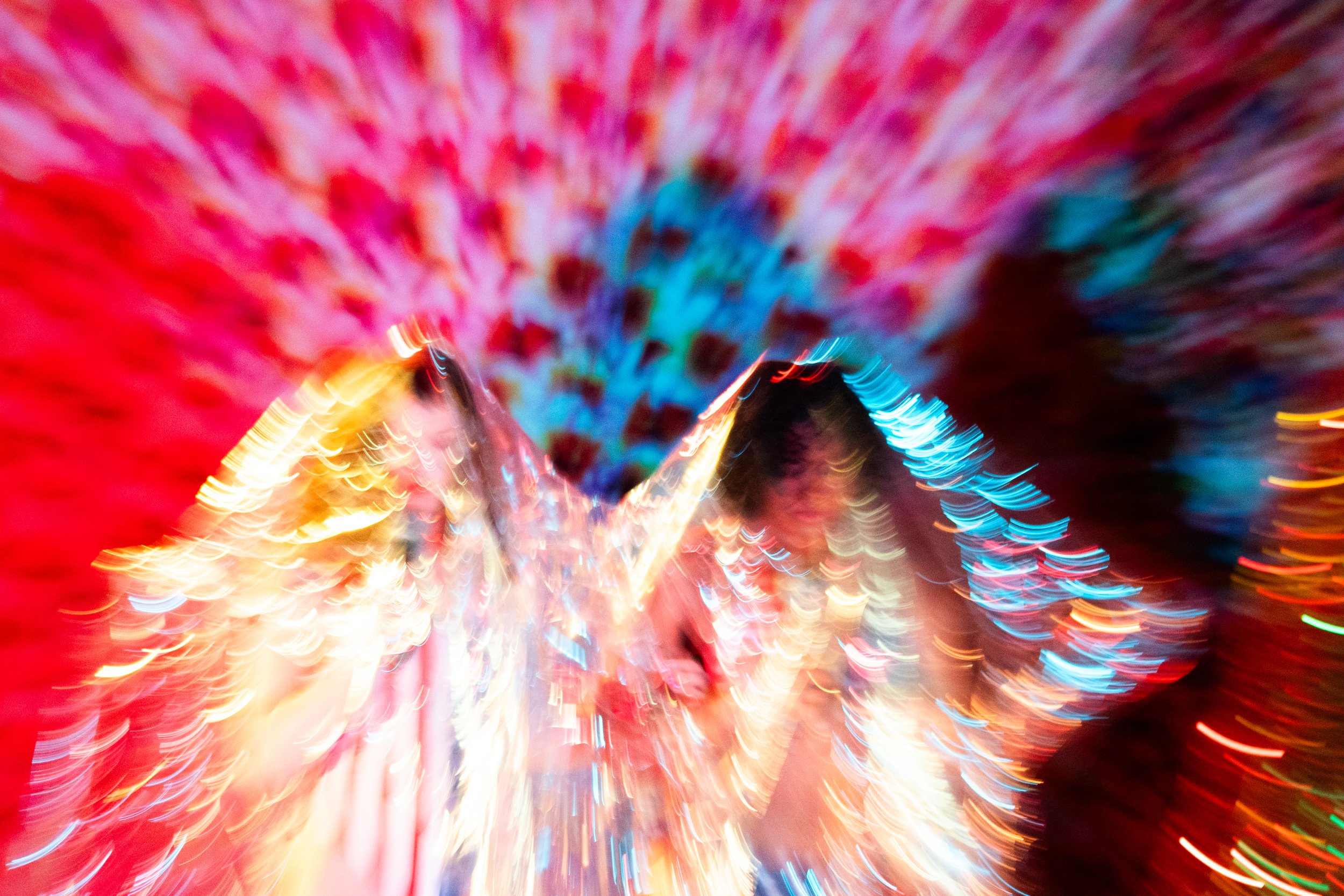 Colorful blurred lights creating a vibrant, swirling pattern with streaks of red, blue, yellow, and other colors, resembling a long-exposure photograph of fireworks or neon lights.