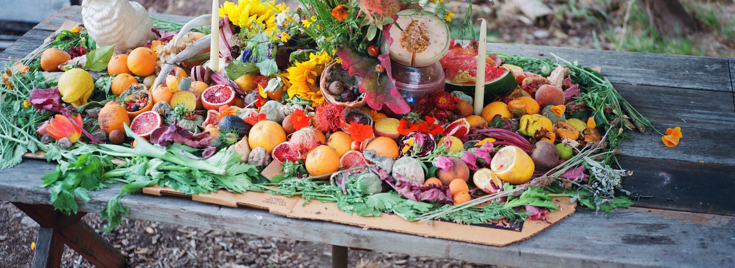 A colorful arrangement of fruits, vegetables, flowers, and candles on a rustic wooden table.