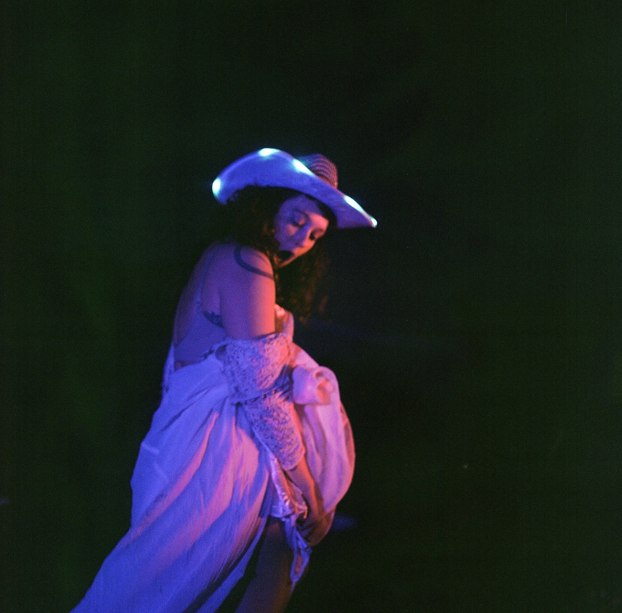 A person wearing a luminous, futuristic helmet with bright blue and purple lights, looking down in a dark environment with minimal background detail.