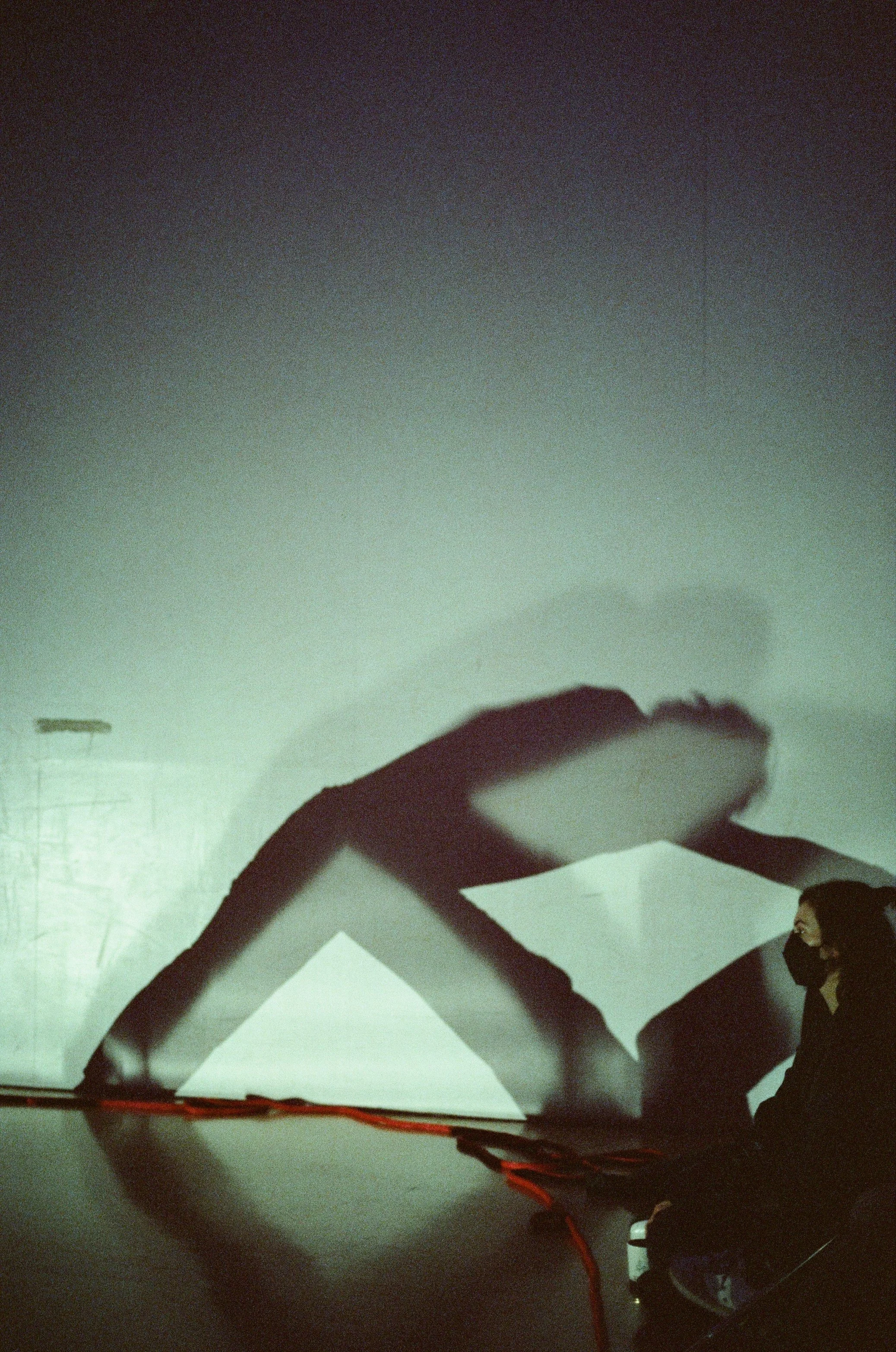 A person with glasses and a face mask examining a 3D geometric shape with a person visible at the bottom right corner.