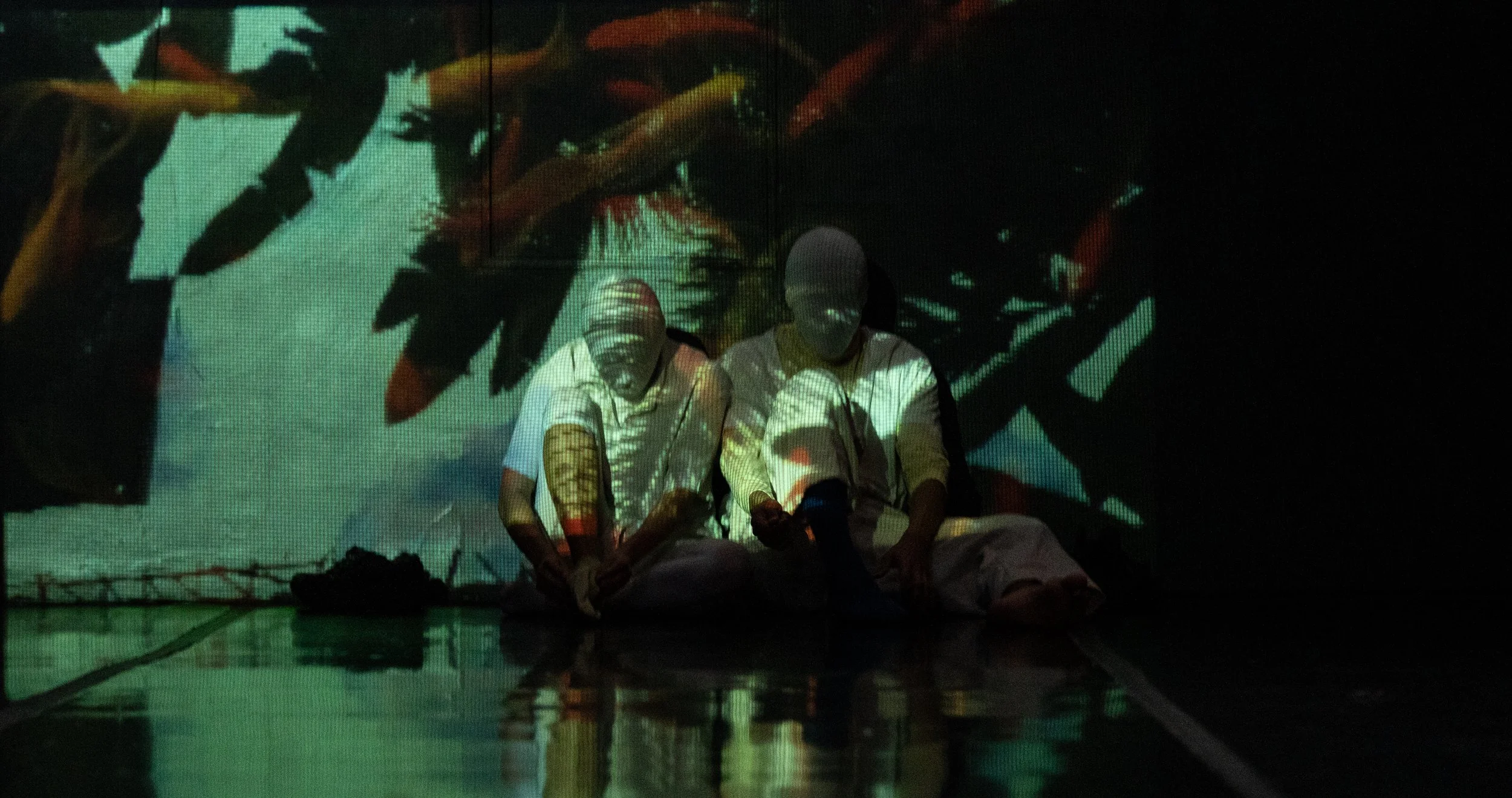 Two individuals sitting on the floor with a colorful abstract projection on the wall behind them.