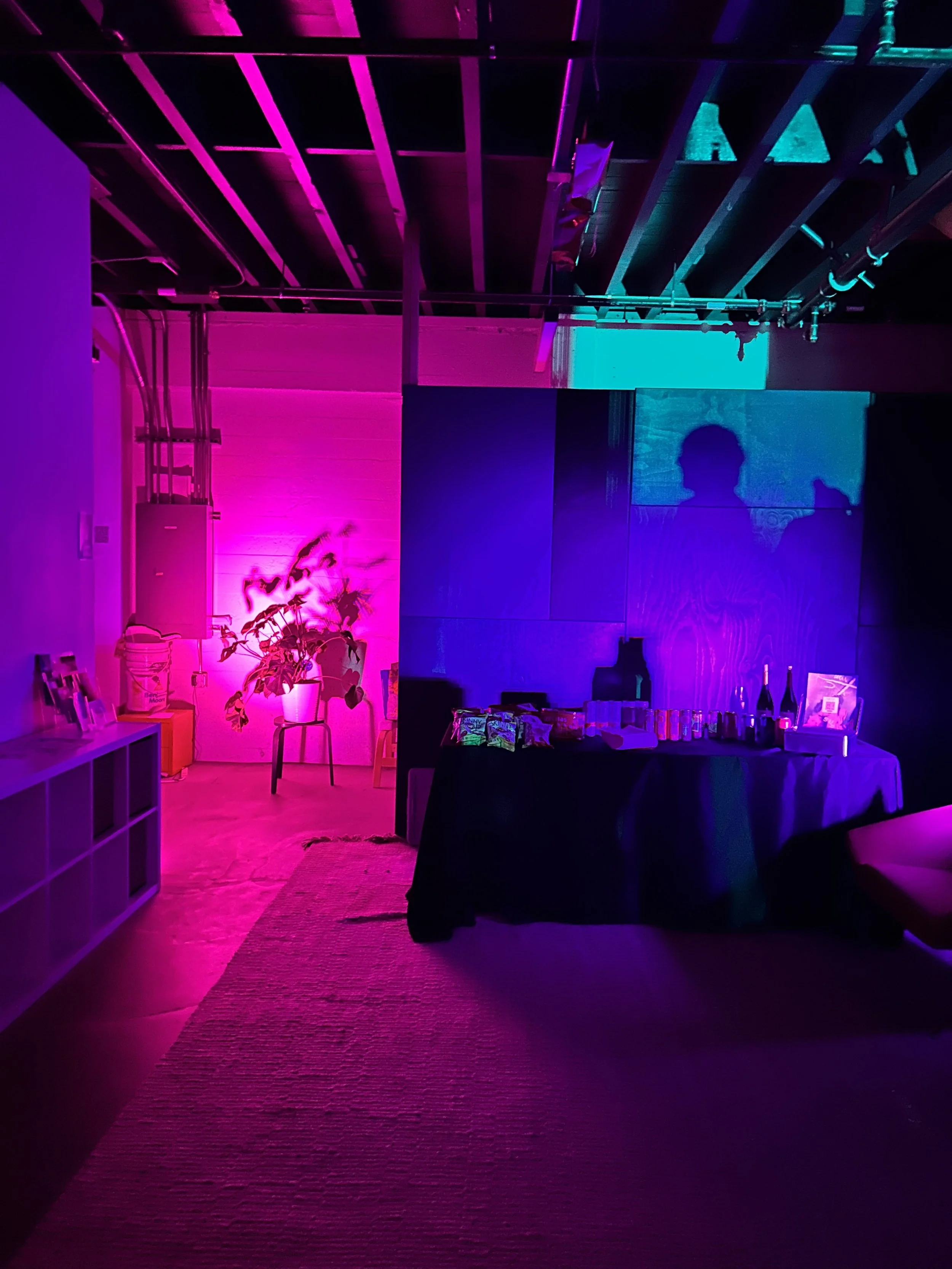 Room with purple and blue lighting, a table with snacks and drinks, and shadows of people projected on the wall.