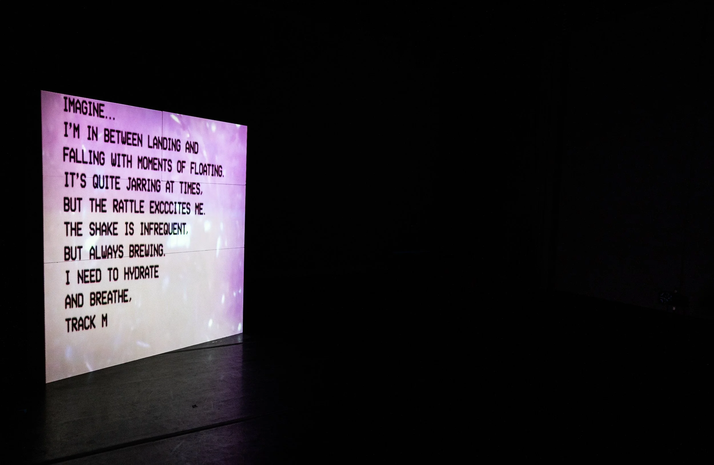 A digital screen displaying a poetic message about floating and brewing, with purple and white star-like background patterns, located in a dark room.