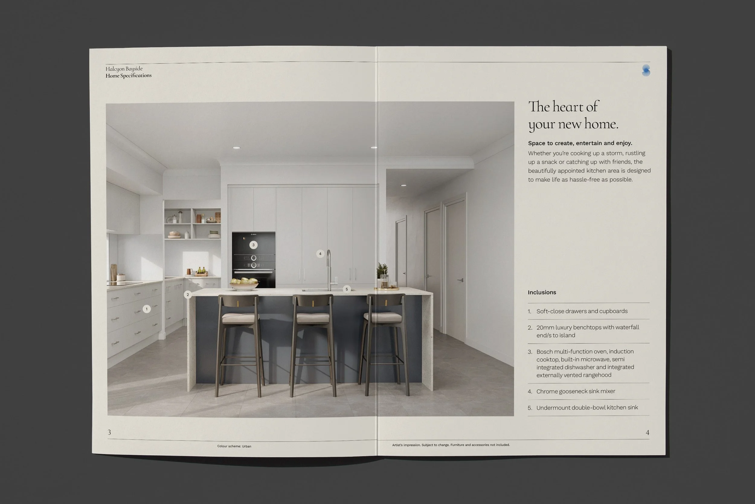 Open magazine showing a modern kitchen with a white island, bar stools, and cabinetry. The right page contains text about home specifications and a small artist's impression of the space.