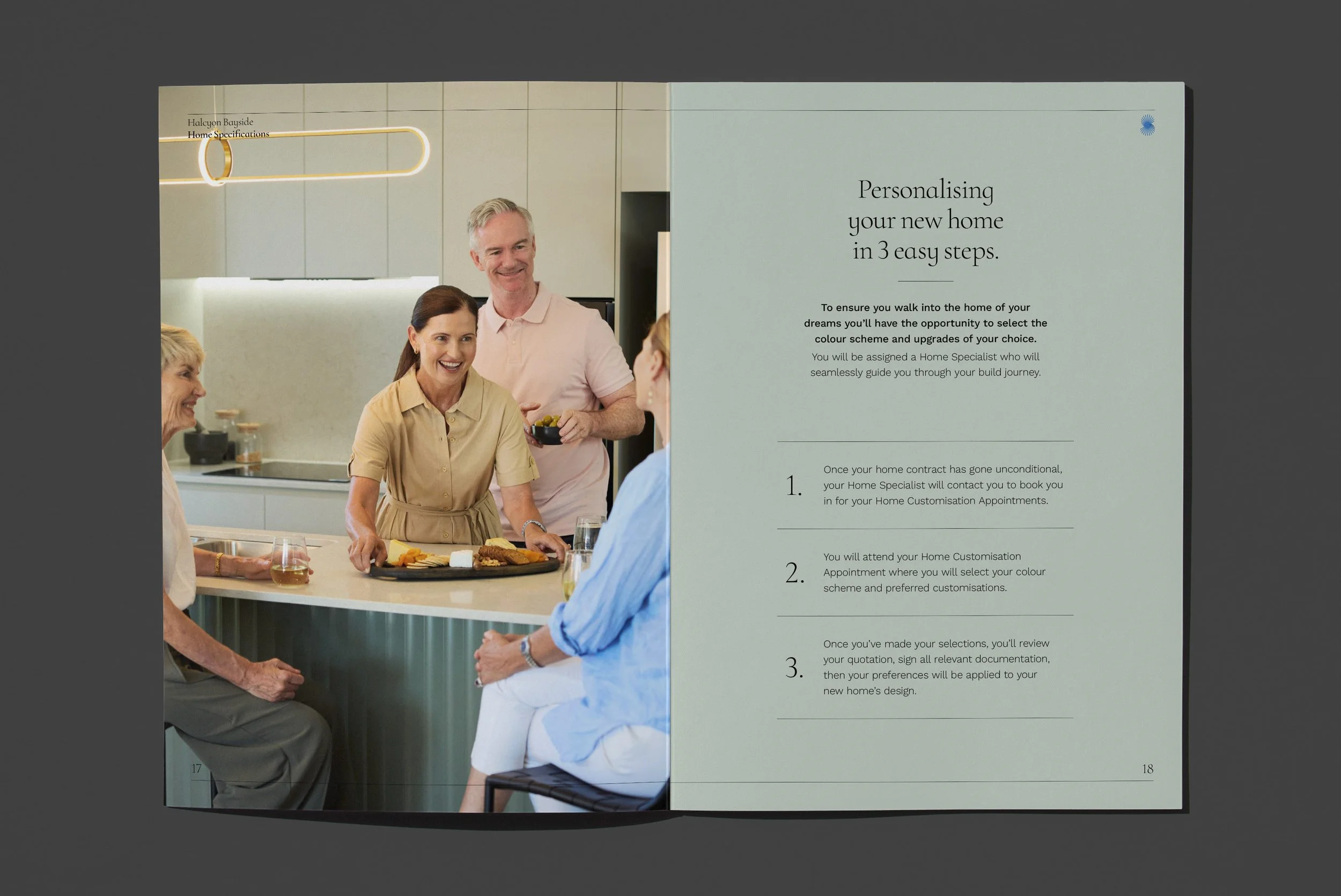 A group of people engaging in a discussion at a kitchen table, with a woman smiling and holding a tray of food, indicating a social or meeting setting inside a modern kitchen with light-colored cabinets and neutral decor.